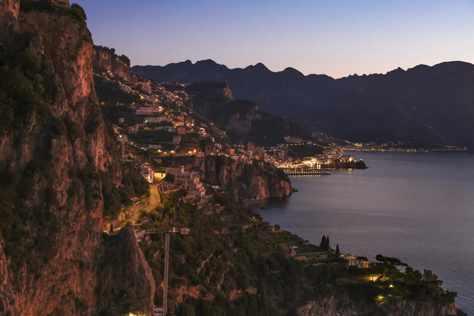 Breathtaking twilight view of the Amalfi Coast, Italy, showcasing illuminated coastal towns and rocky landscape.