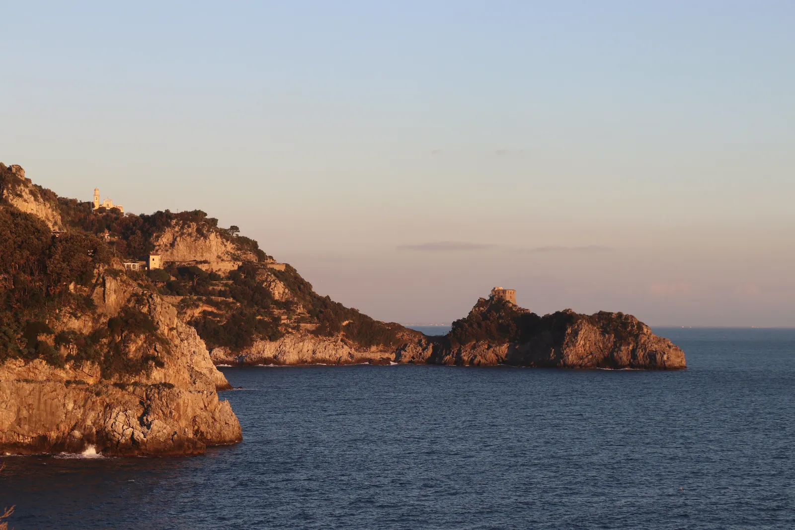 Dramatic cliffs meet tranquil sea at Praiano's coastline during sunset.