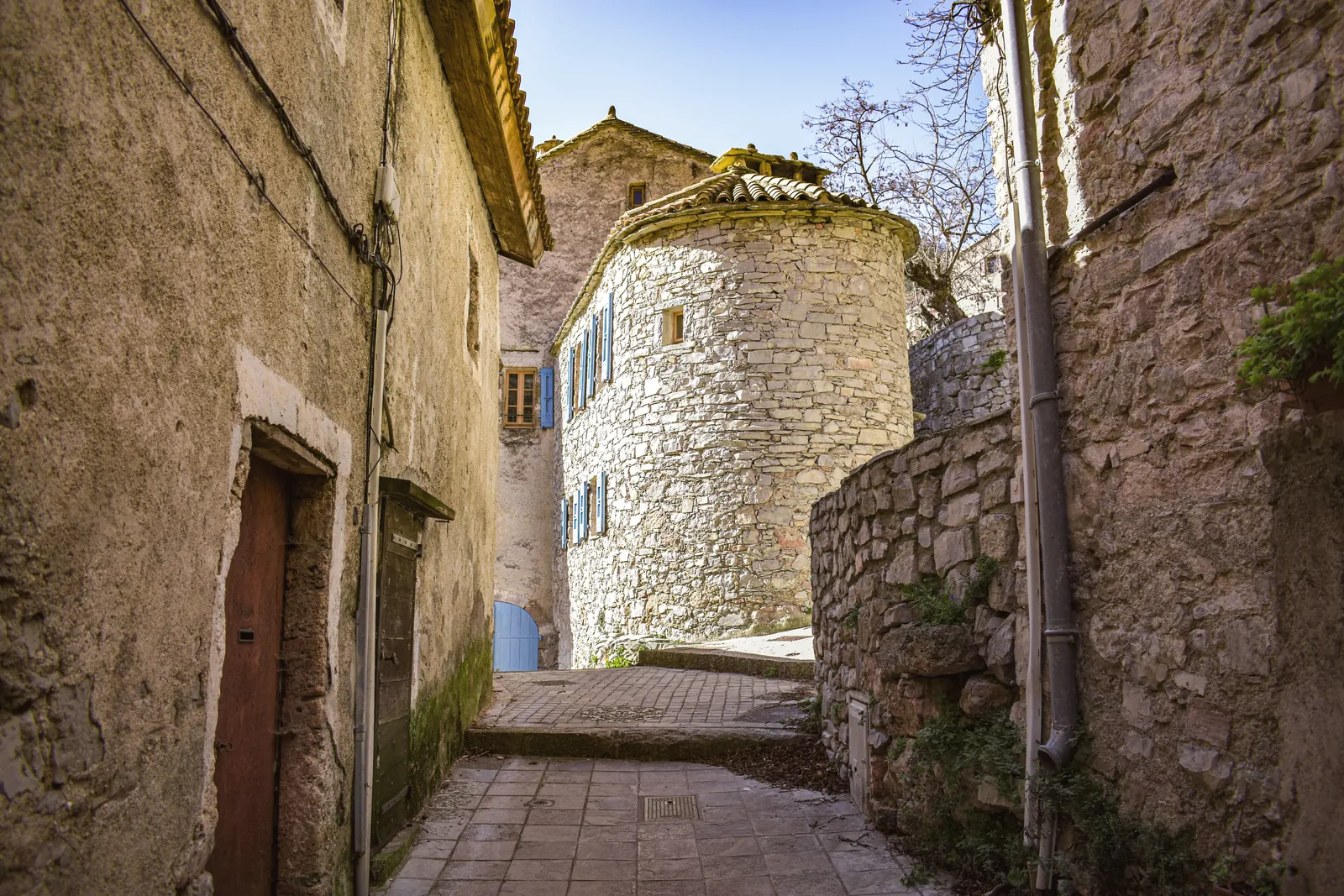 Picturesque alleyway in a French village with stone buildings and blue shutters.