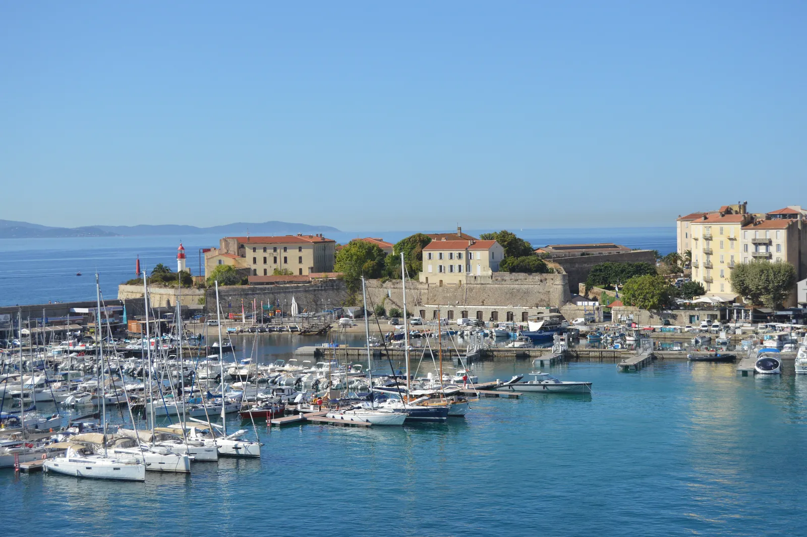 Explore the tranquil coastal scene with sailboats docked near historic architecture under a clear blue sky.