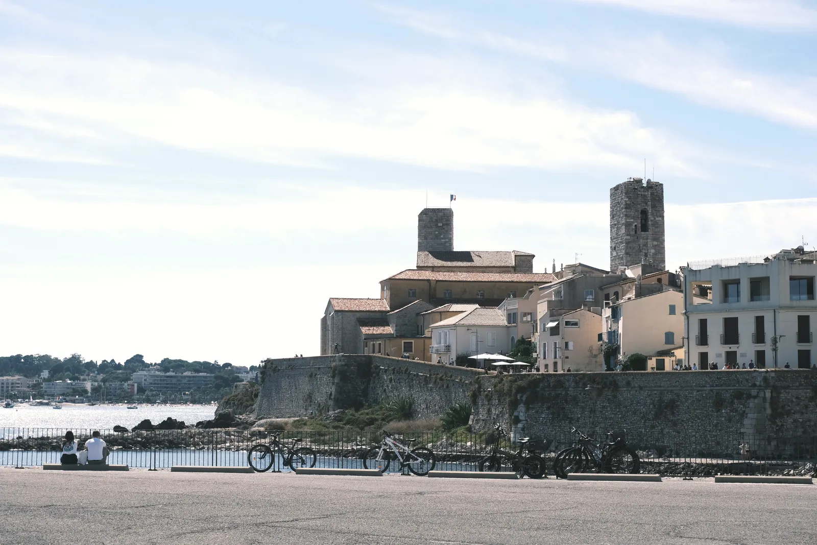 View of historic Antibes with prominent fort tower by the sea, bicycles in foreground.