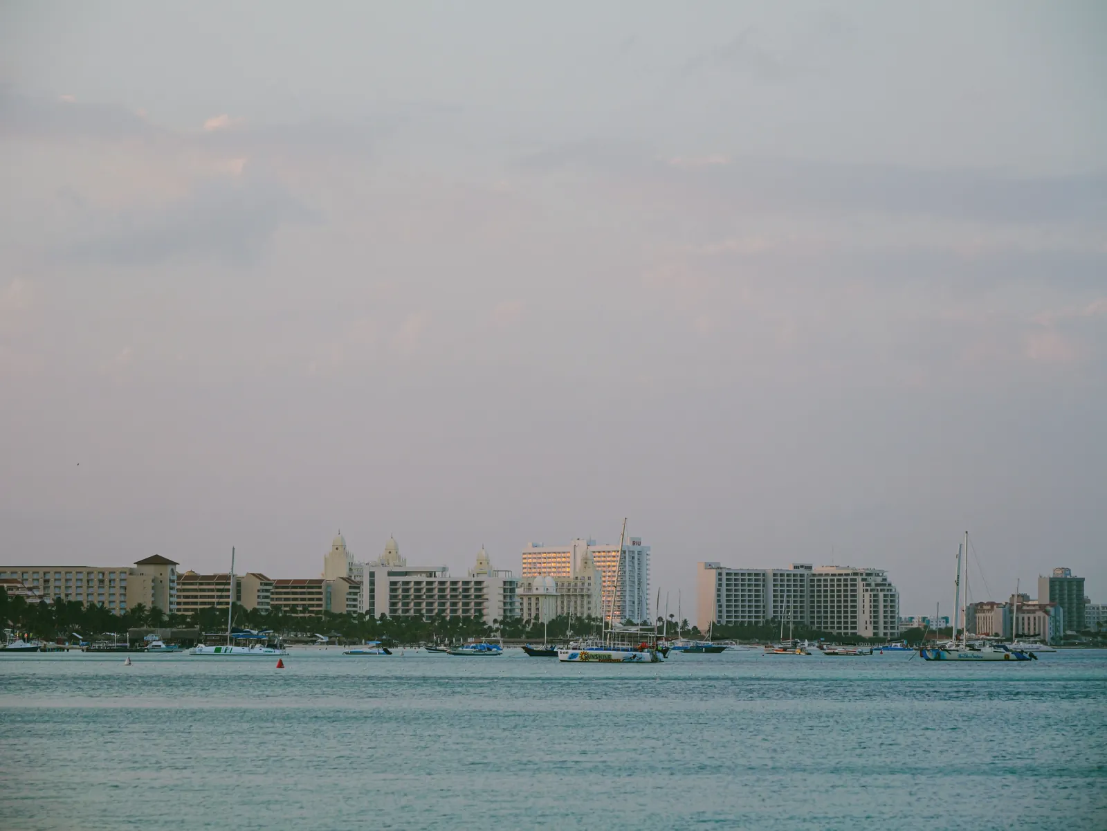 A serene view of a coastal cityscape with boats and buildings at twilight, under a pastel sky.