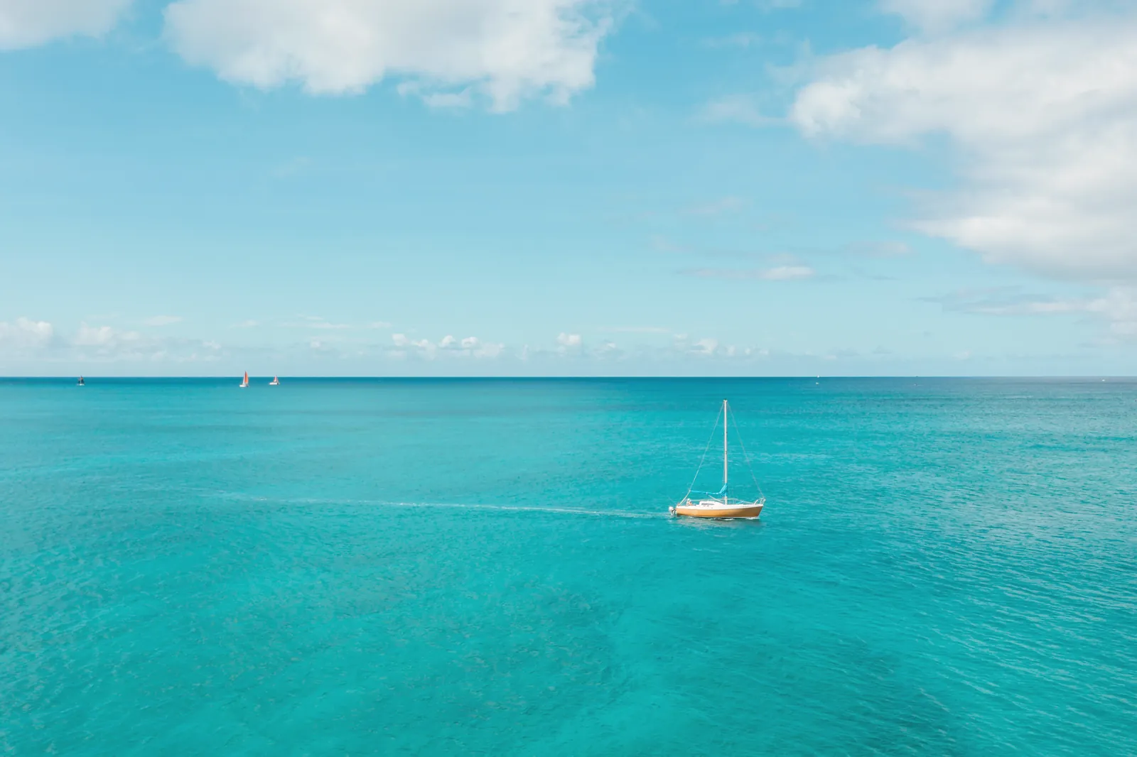 A single sailboat glides on a calm turquoise sea under a bright blue sky.