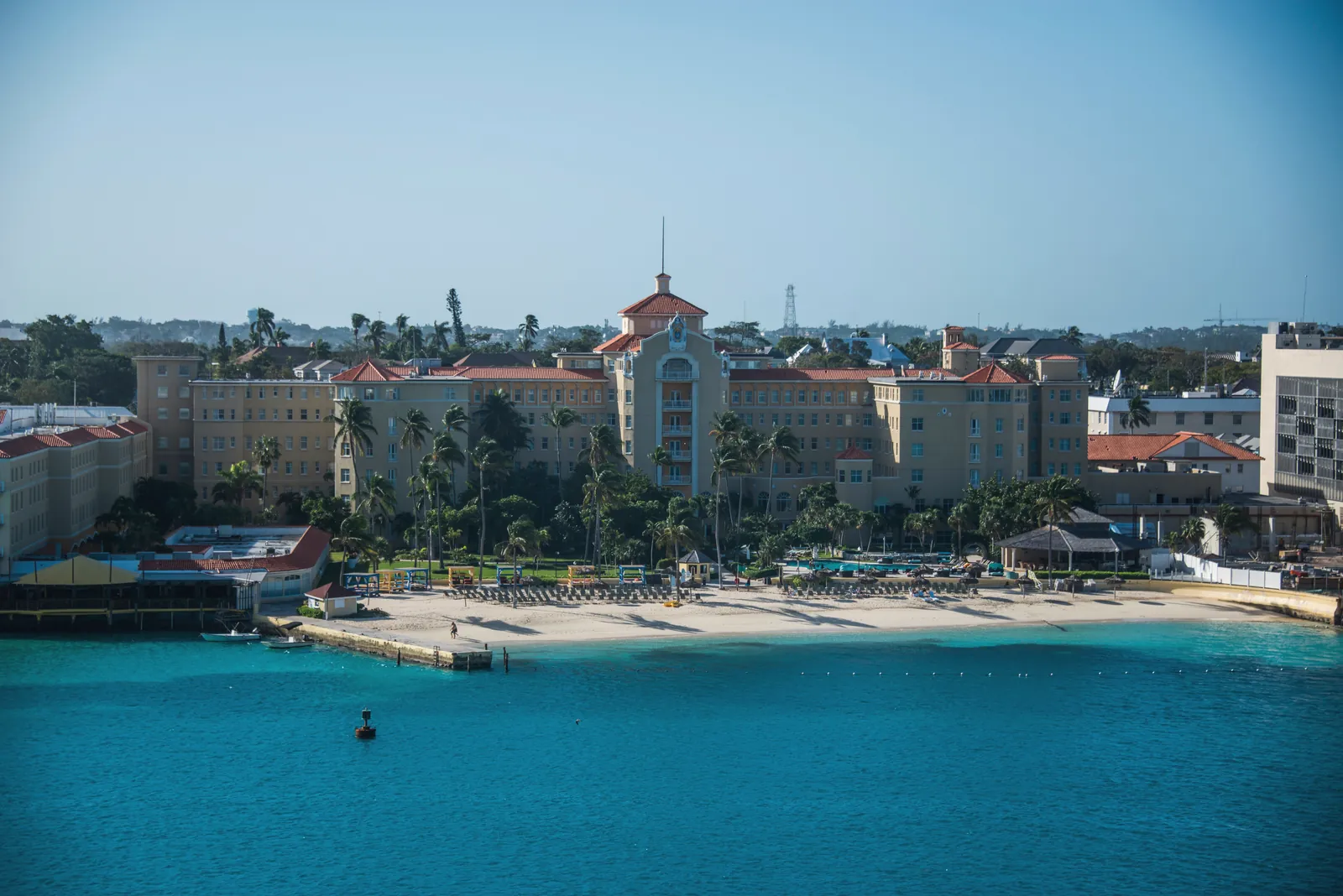 Scenic aerial view of a luxurious hotel by a beautiful turquoise beach under a clear blue sky.