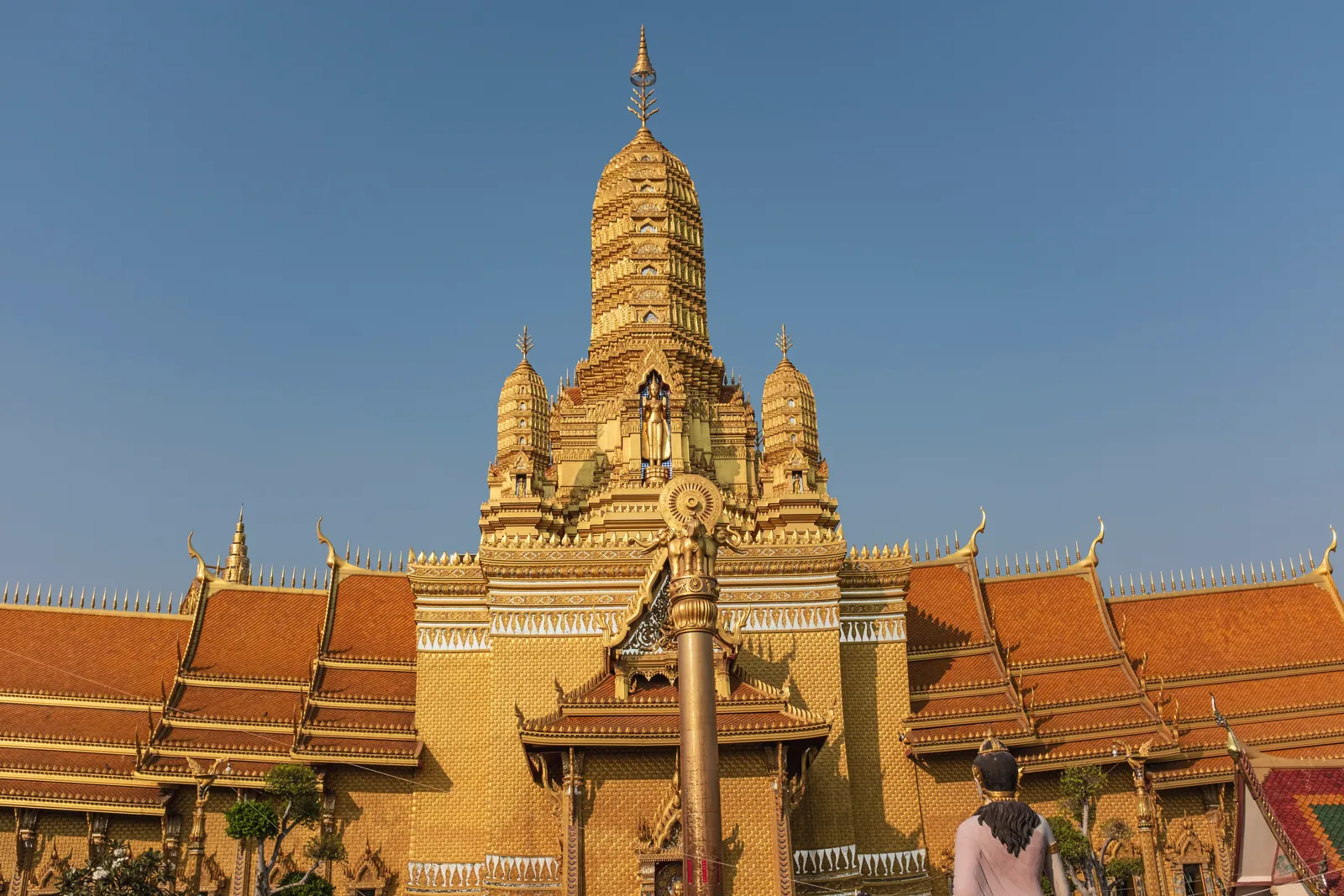 A magnificent golden Buddhist temple in Bangkok against a clear sky, showcasing intricate architecture.