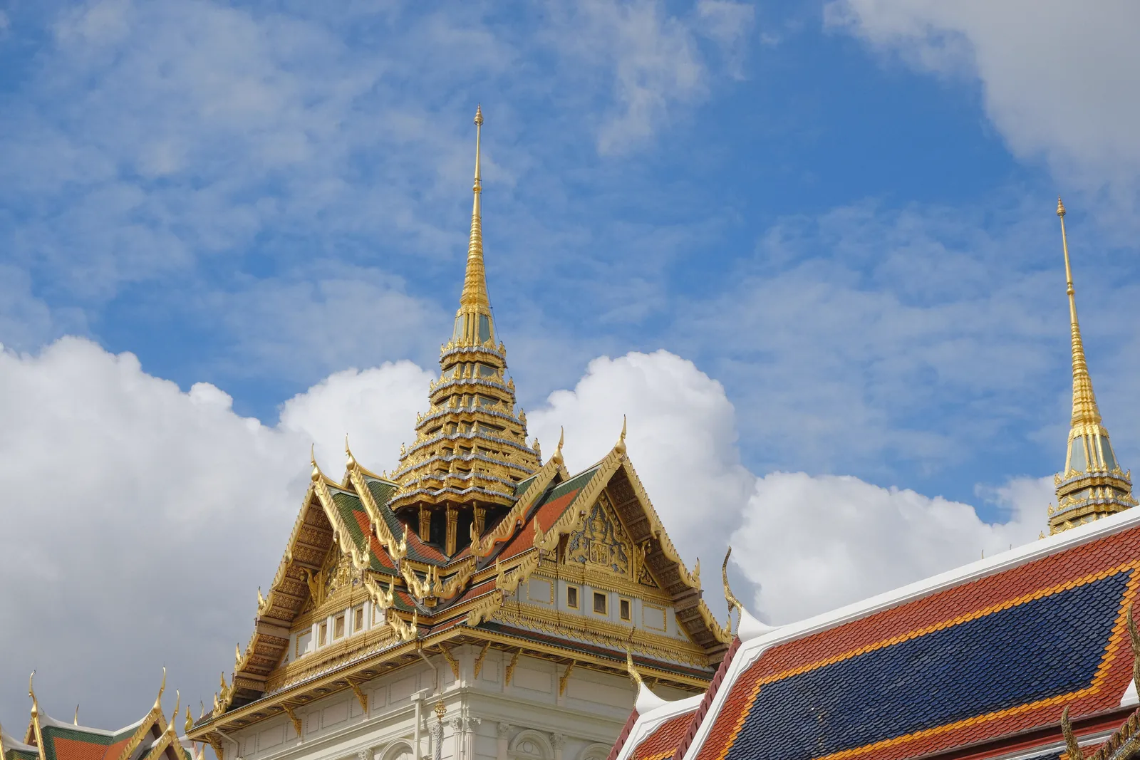 Majestic roof of the Grand Palace with golden spires under a vibrant blue sky in Bangkok, Thailand.