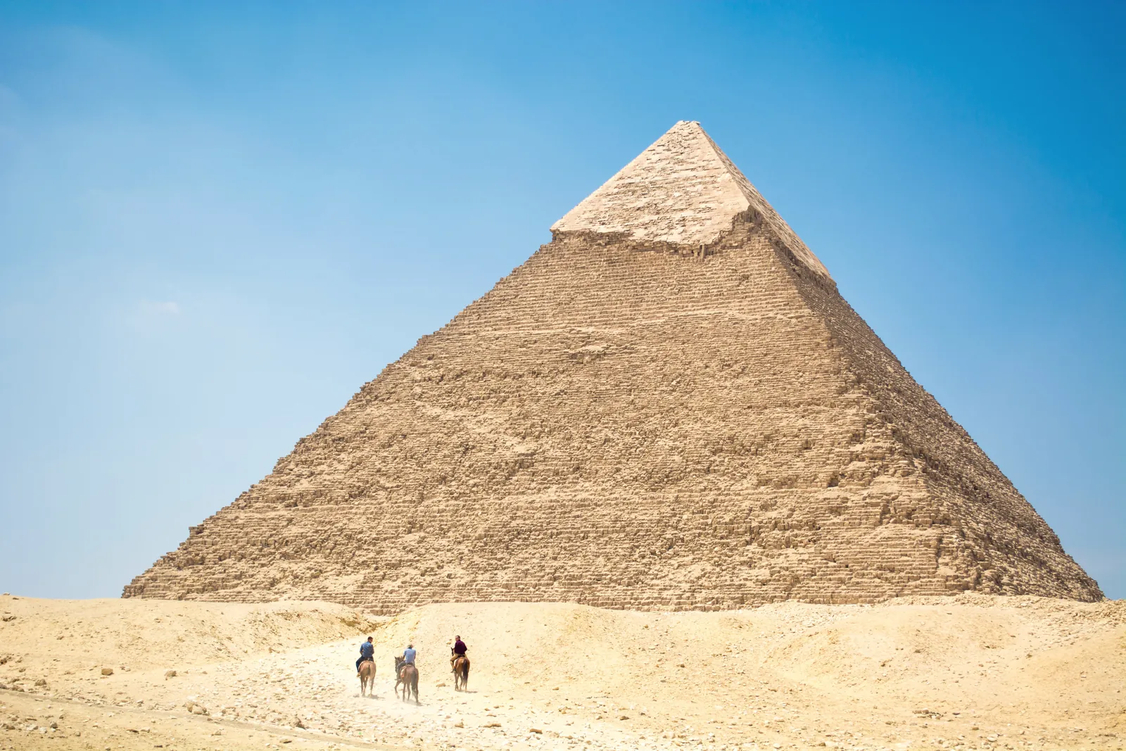 Iconic Giza Pyramid with riders on camels under bright daylight, capturing Egyptian desert landscapes.