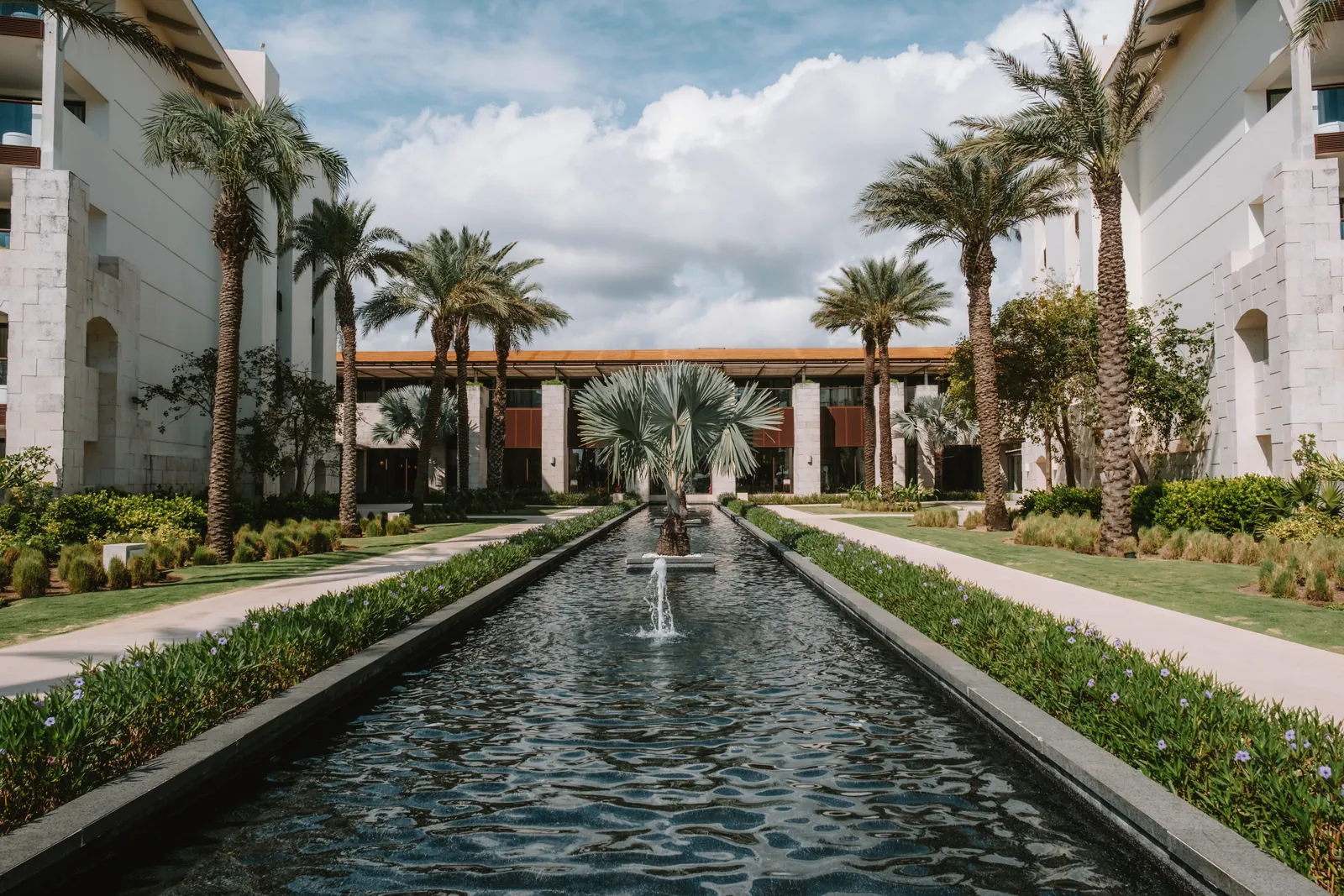 Elegant view of a luxury resort in Quintana Roo, Mexico, featuring palm trees and a serene water feature.