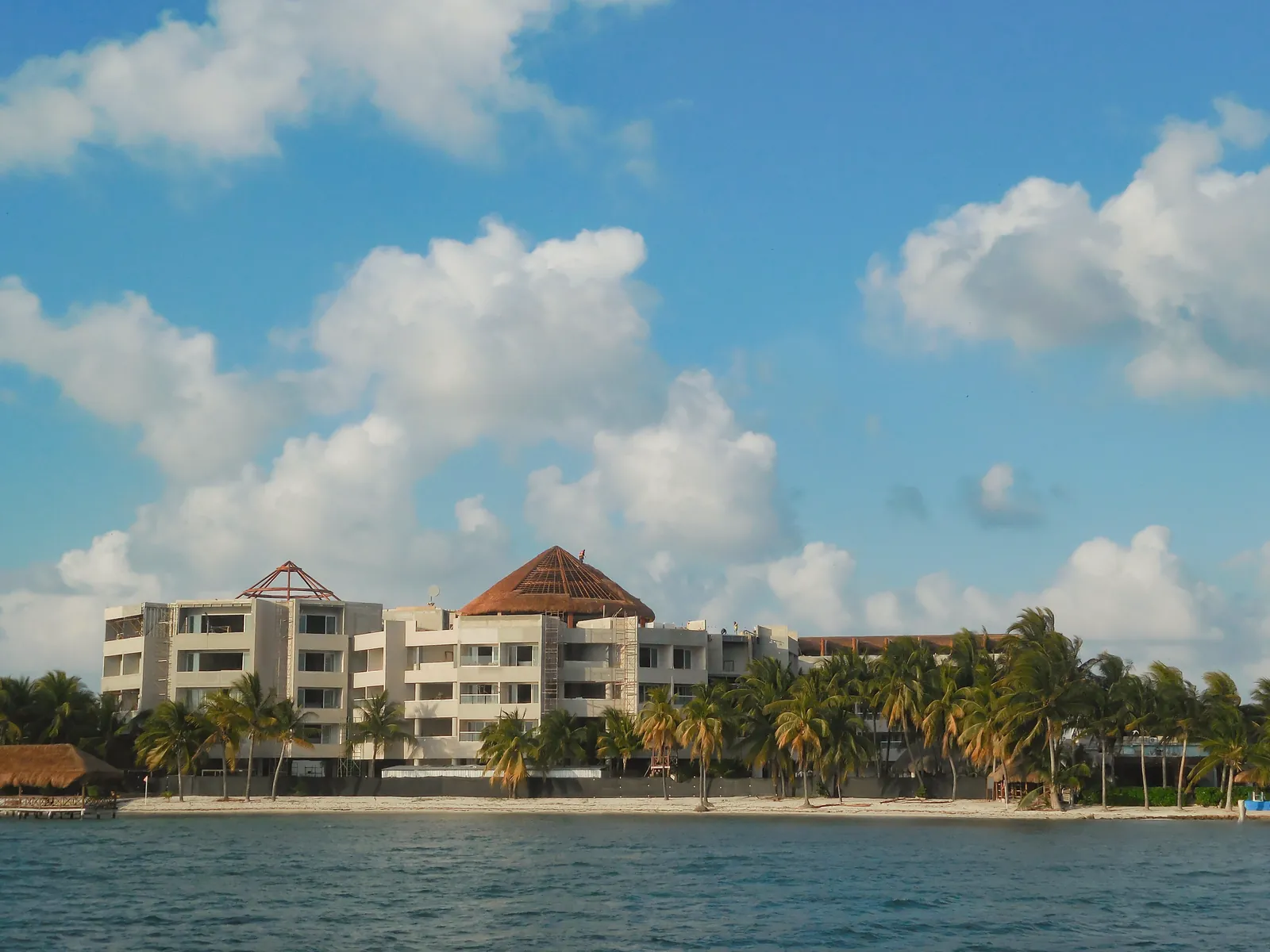 Luxury beachfront resort with palm trees and ocean view under a bright blue sky.