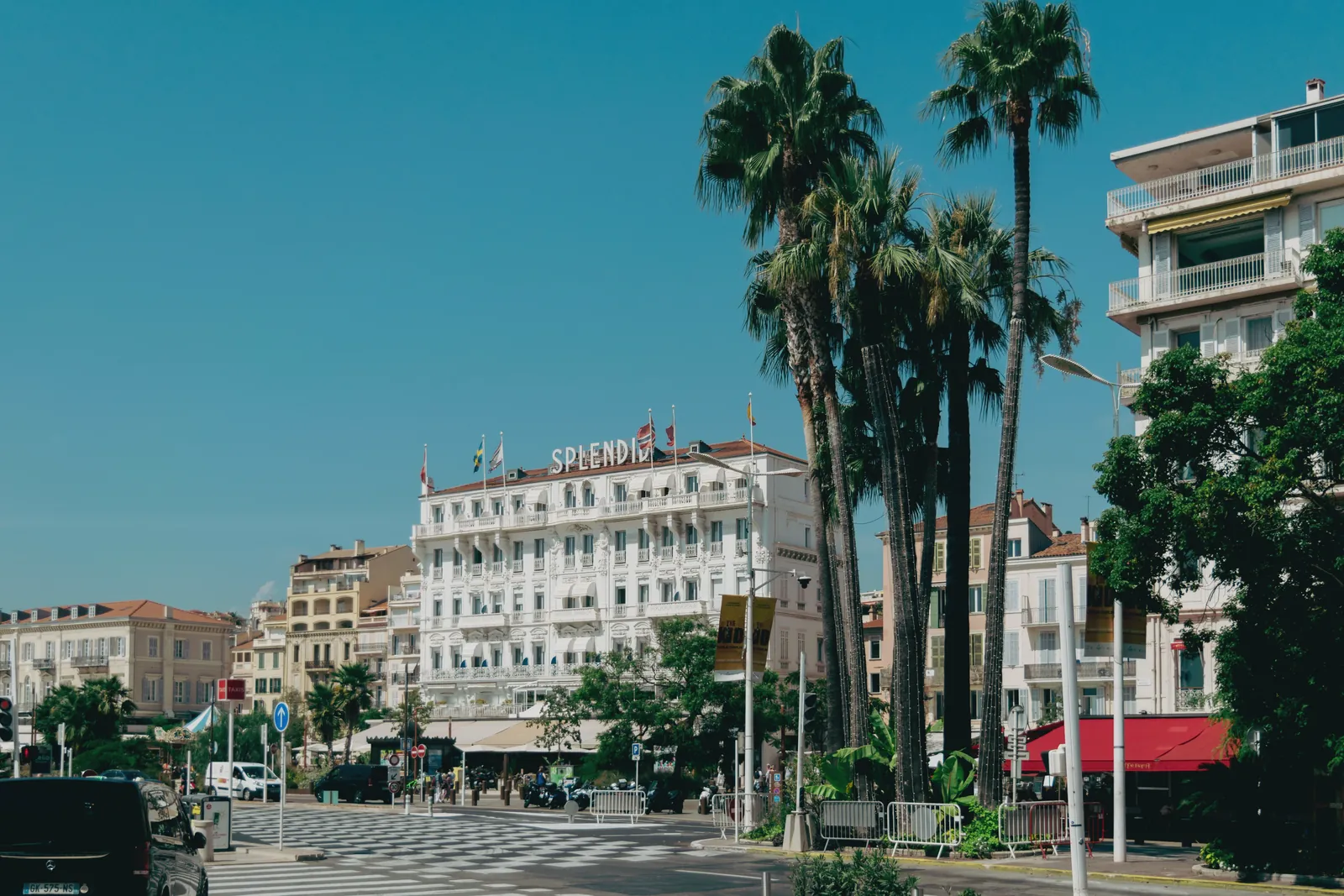 View of the iconic Splendid Hotel in Cannes amidst palm trees on a sunny day.