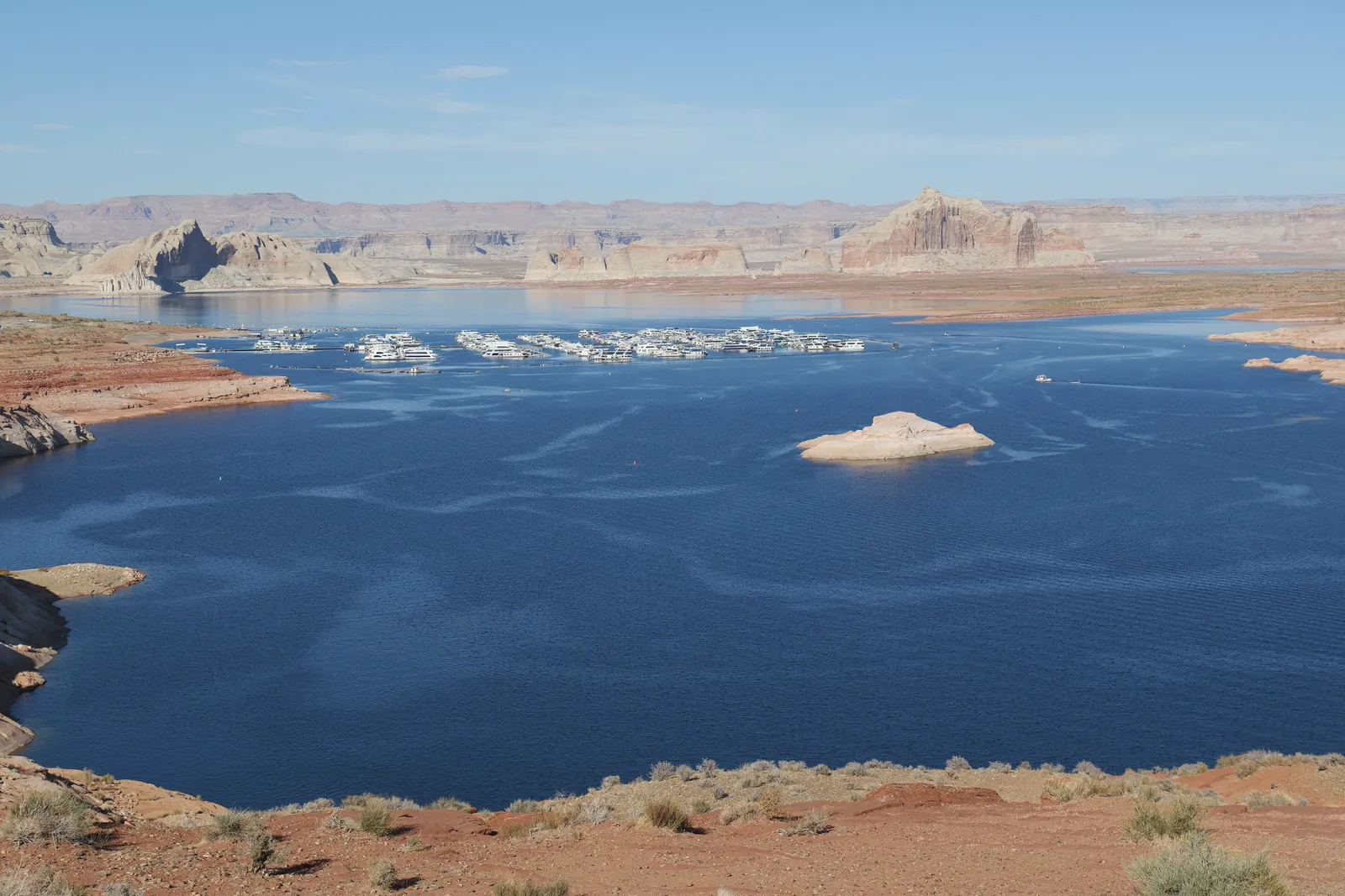 A stunning view of Lake Powell, displaying vibrant blue water, red rocky shores, and houseboats under a clear sky.