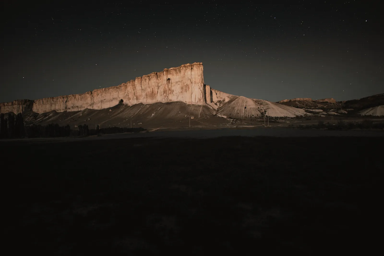 Panoramic view of a starry night sky over a rugged rocky cliff, highlighting natural beauty.