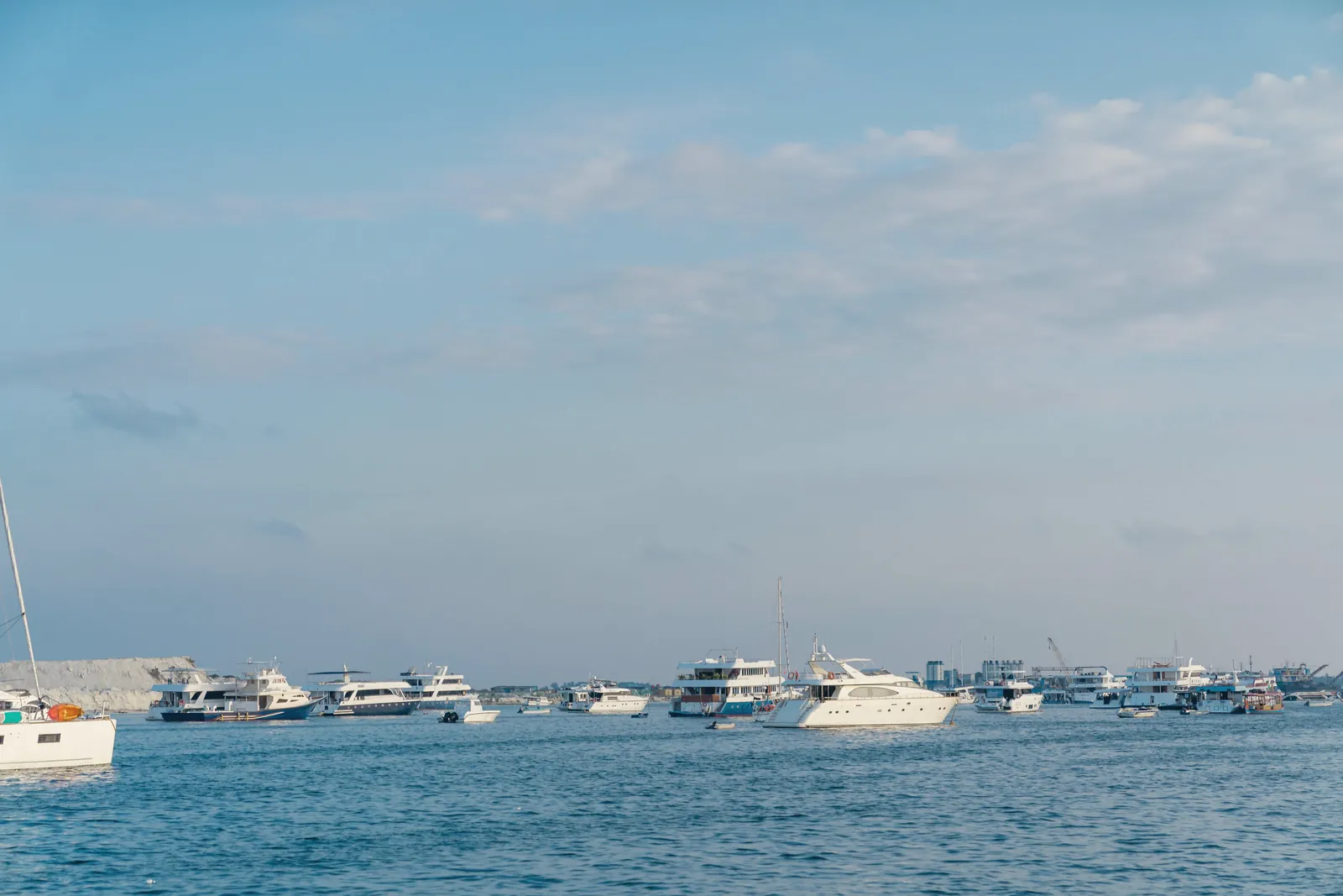 A fleet of luxury yachts anchored in a tranquil ocean harbor under a clear sky.
