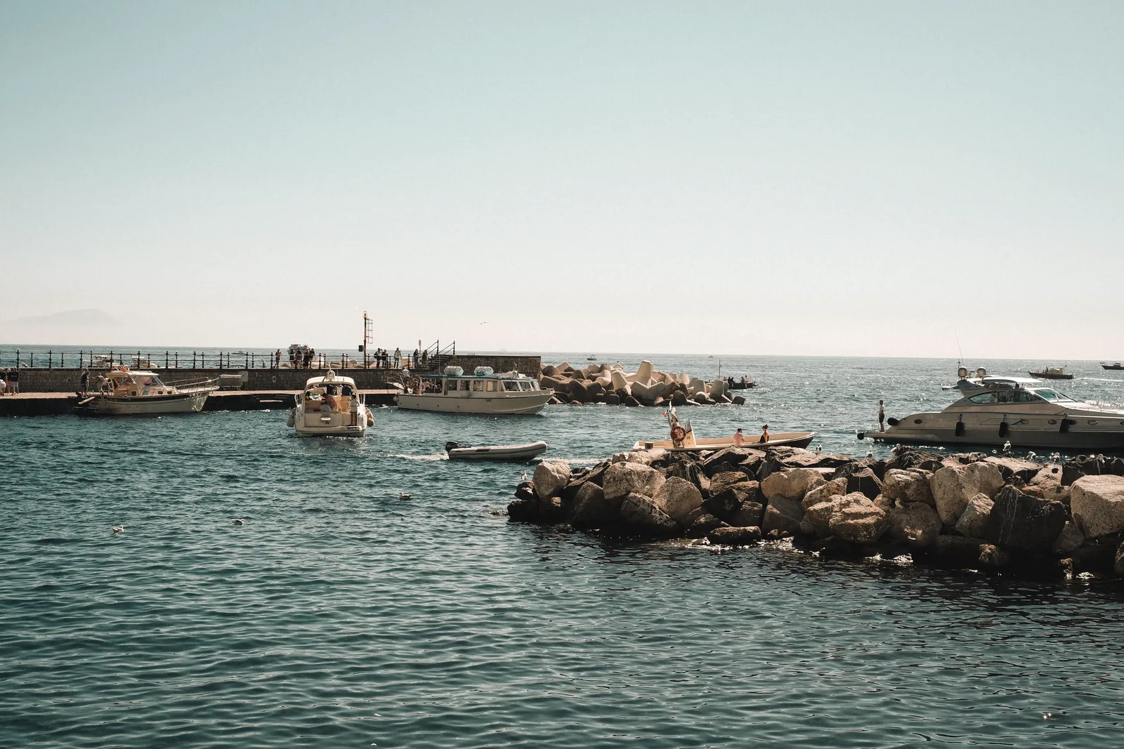 A picturesque view of boats in a marina with rocky seashore on a sunny day.