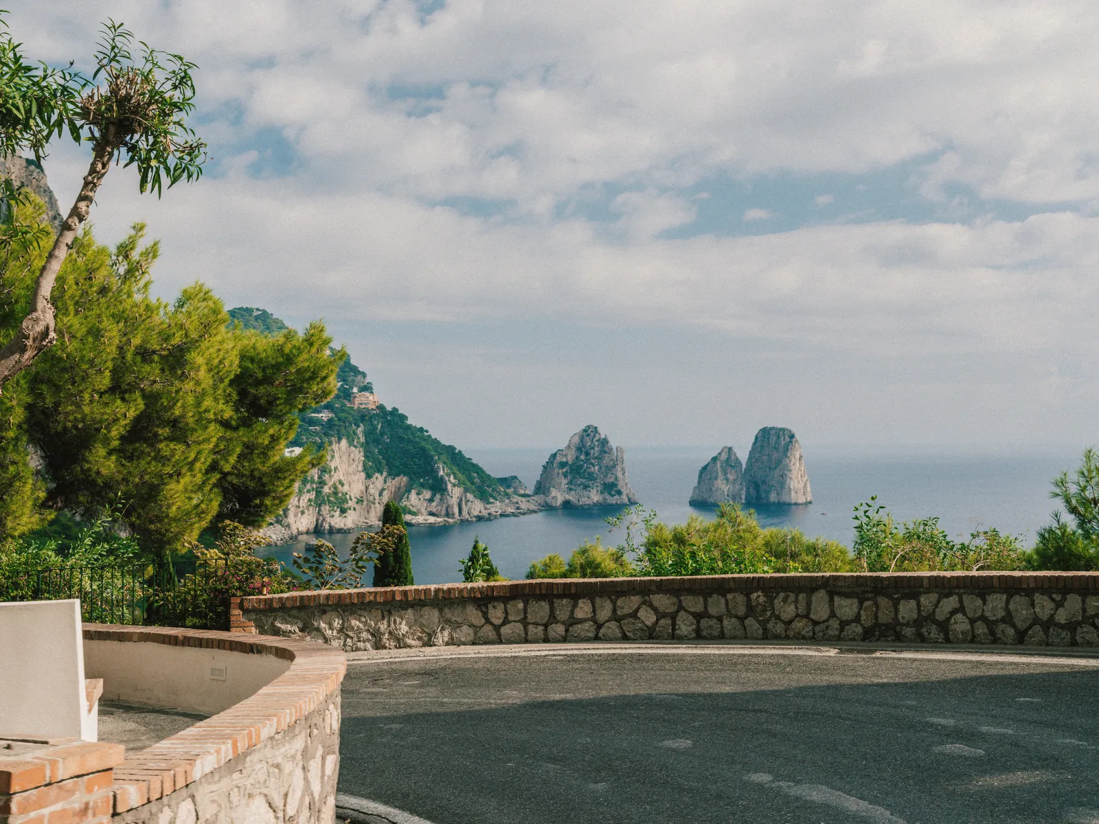 Stunning view of Faraglioni rock formations off the coast of Capri, Italy with lush greenery in the foreground.