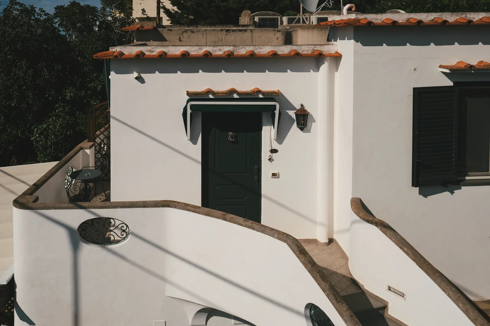 Charming Mediterranean-style house facade with distinct curved stucco staircase during a sunny day.