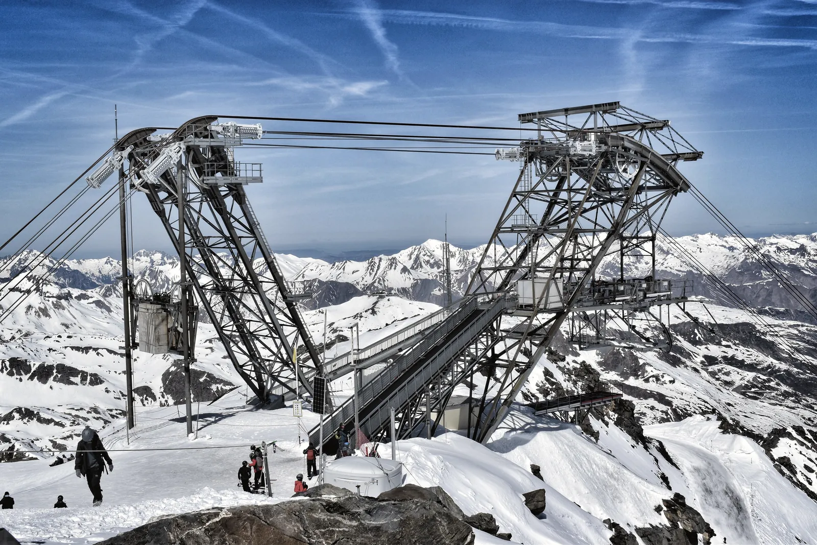 A scenic aerial tramway set against stunning snow-capped mountains under a clear blue sky.