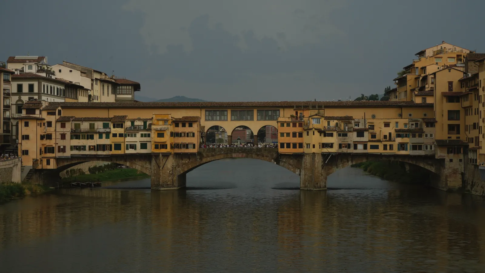 Iconic Ponte Vecchio in Florence, Italy, with overcast sky reflection.