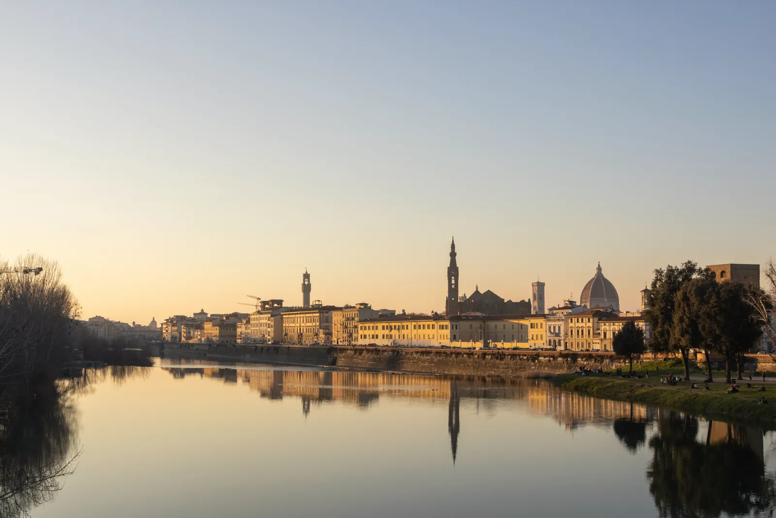 Peaceful sunset view of Florence skyline with the Arno River reflecting historic architecture.