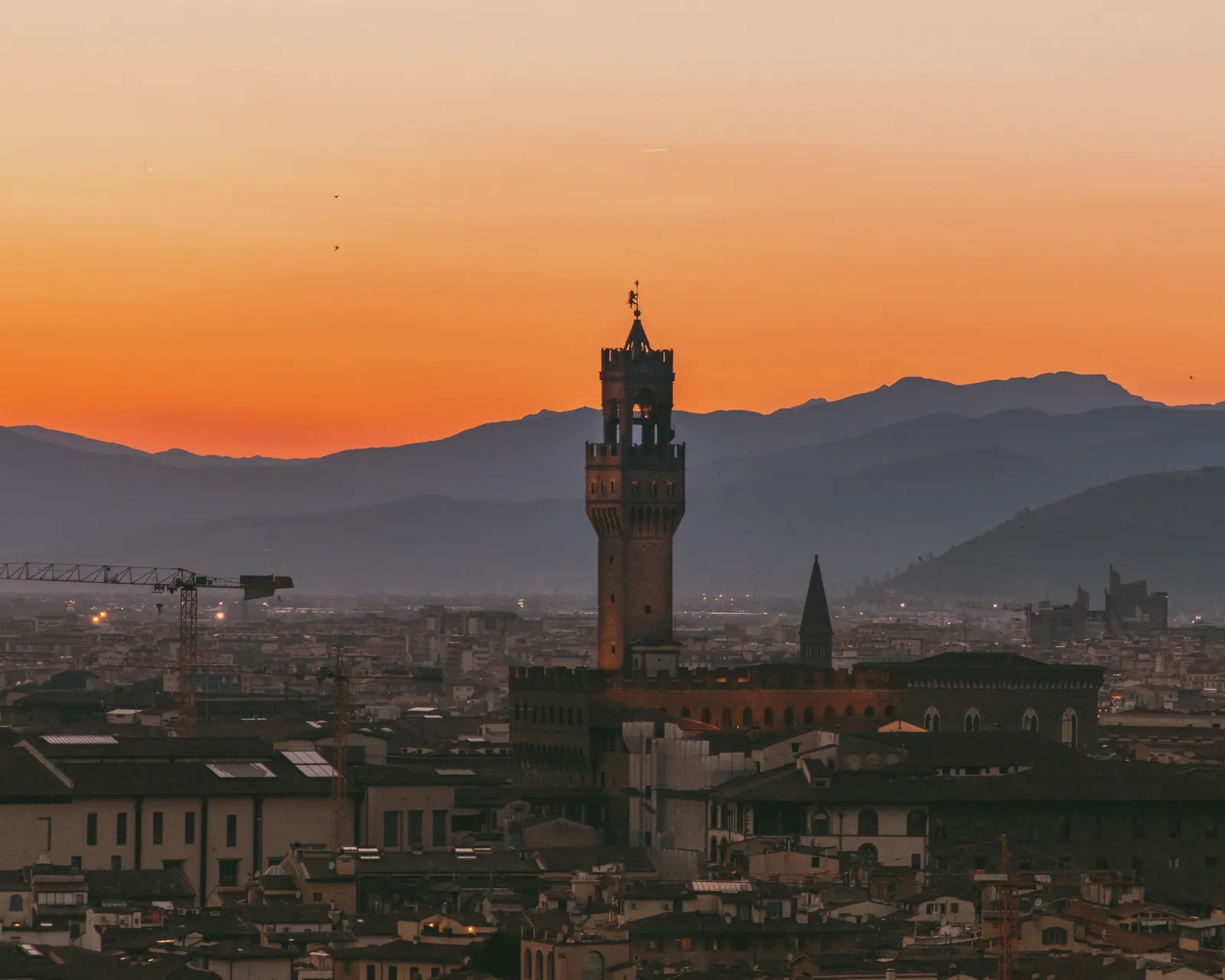 Stunning view of Florence and Palazzo Vecchio against an orange sunset sky in Tuscany, Italy.