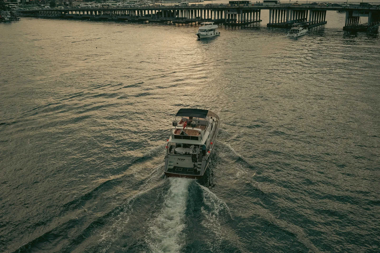Drone shot of a yacht cruising through calm waters near a pier in the evening light.