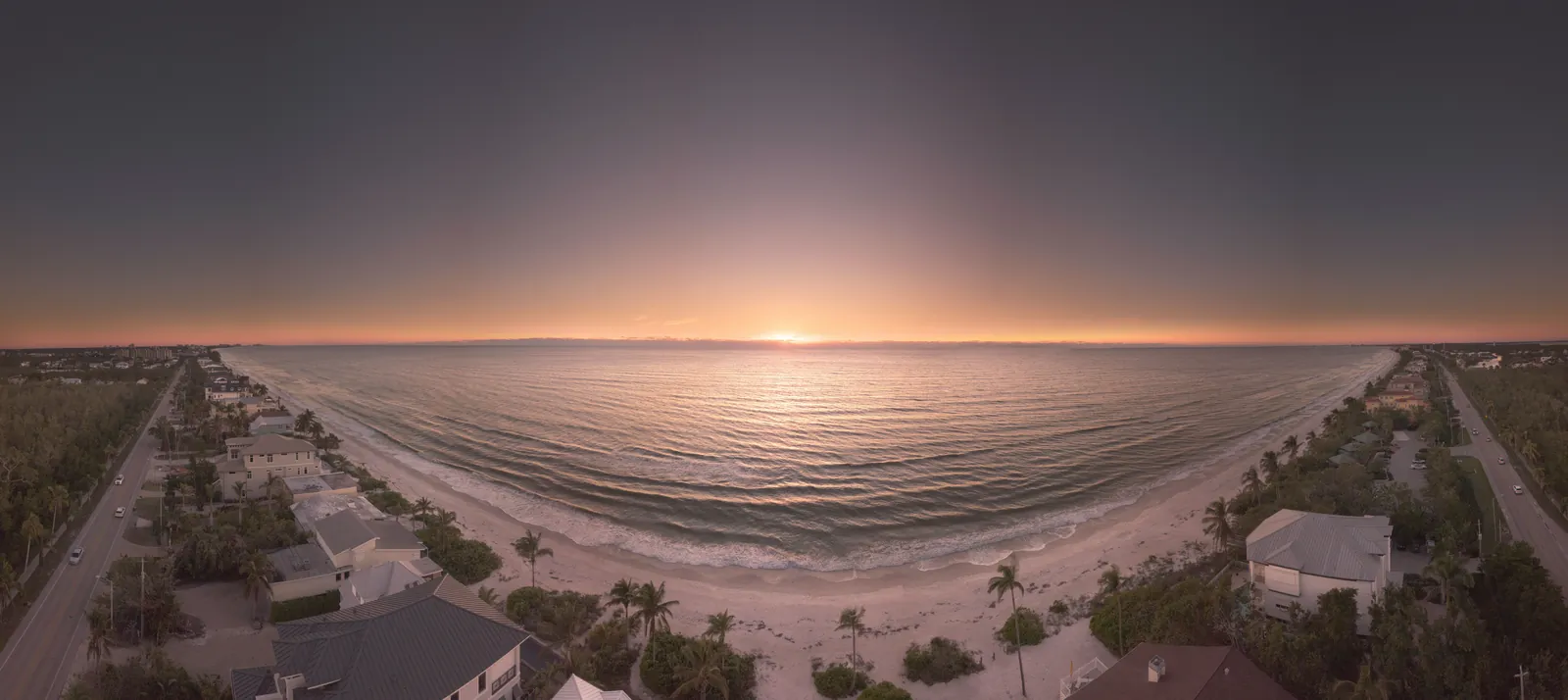 A stunning aerial panorama capturing a serene beach sunset with houses lining the shore.