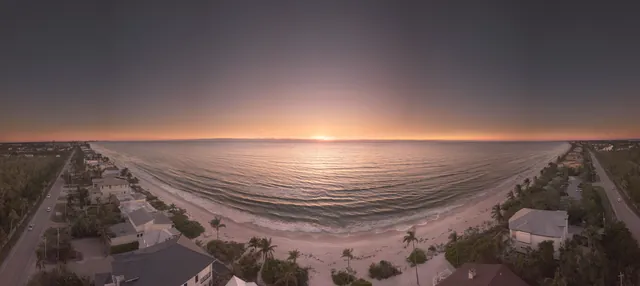 A stunning aerial panorama capturing a serene beach sunset with houses lining the shore.