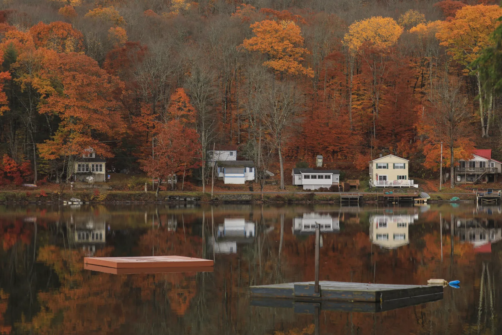 Charming autumn landscape with houses reflecting in a serene lake in Catskill, NY.