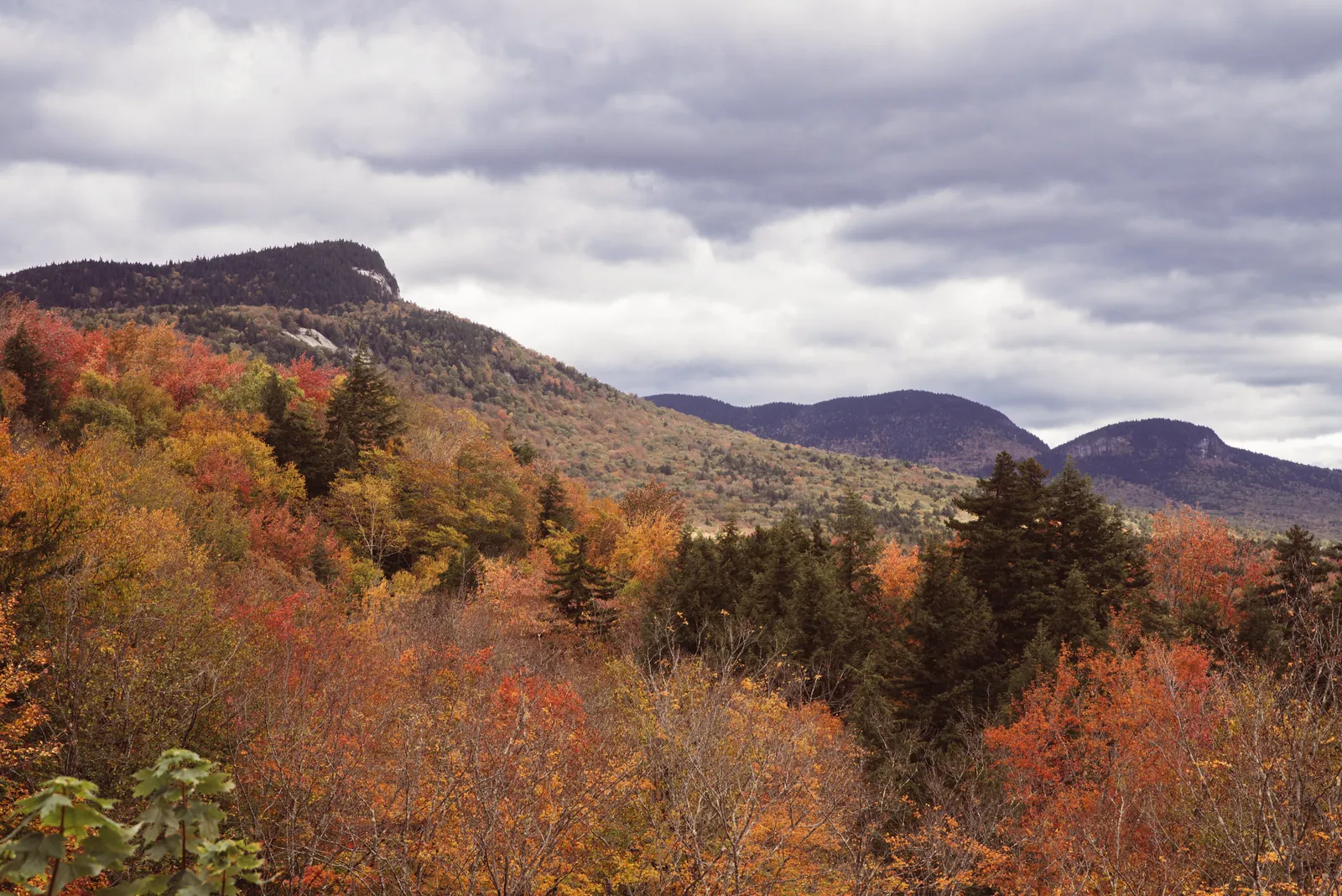Vibrant fall foliage in a stunning mountain landscape under a dramatic cloudy sky.