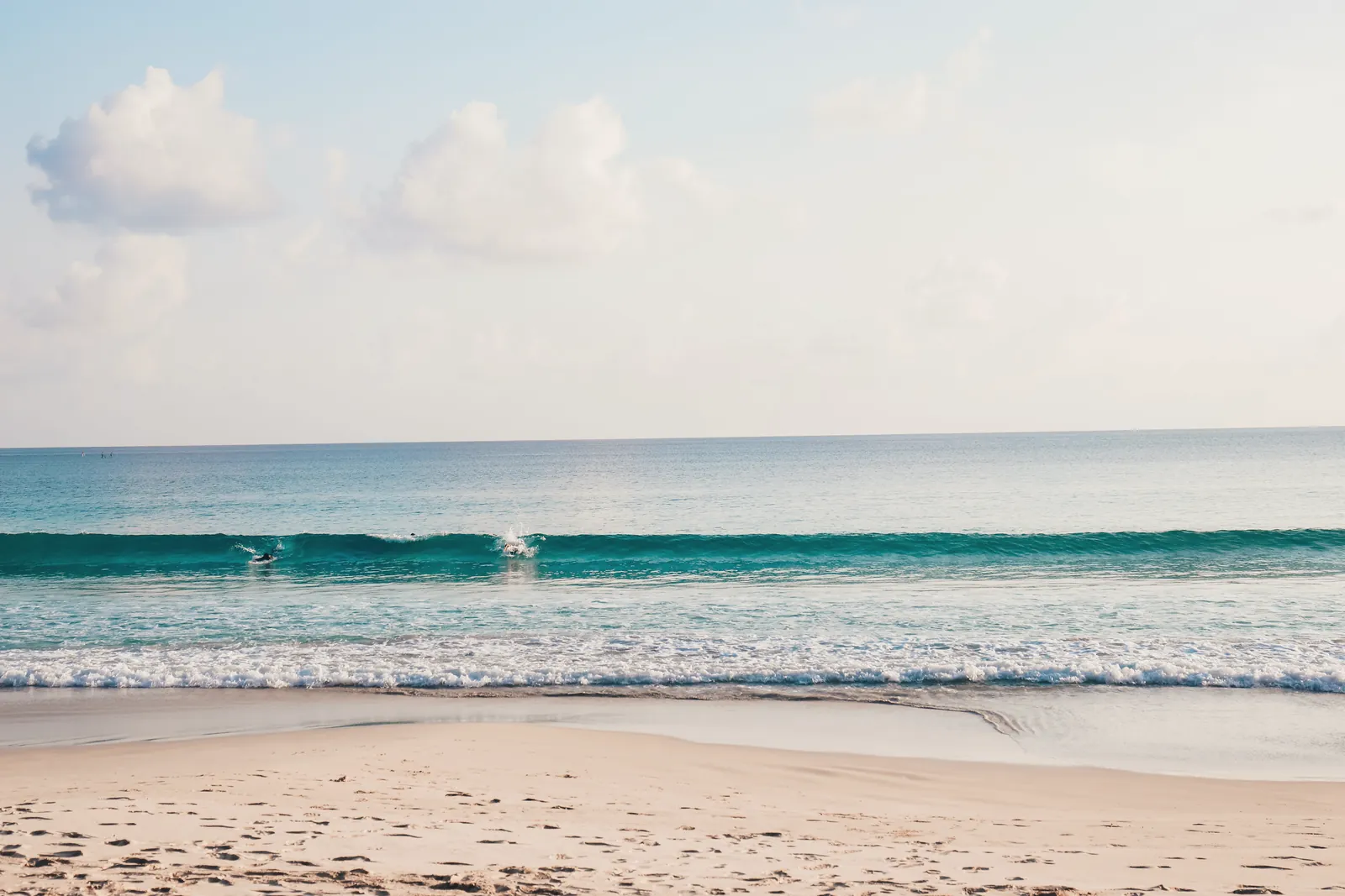 Picturesque view of foamy ocean near sandy beach with footprints under cloudy sky with horizon
