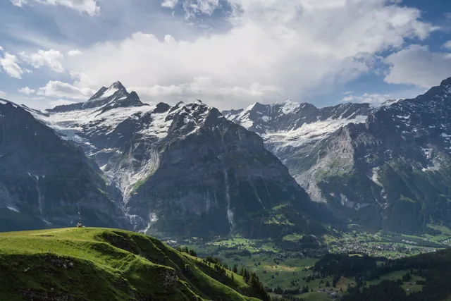 Panoramic view of the Swiss Alps in the Jungfrau region with lush green valleys and snow-capped peaks.