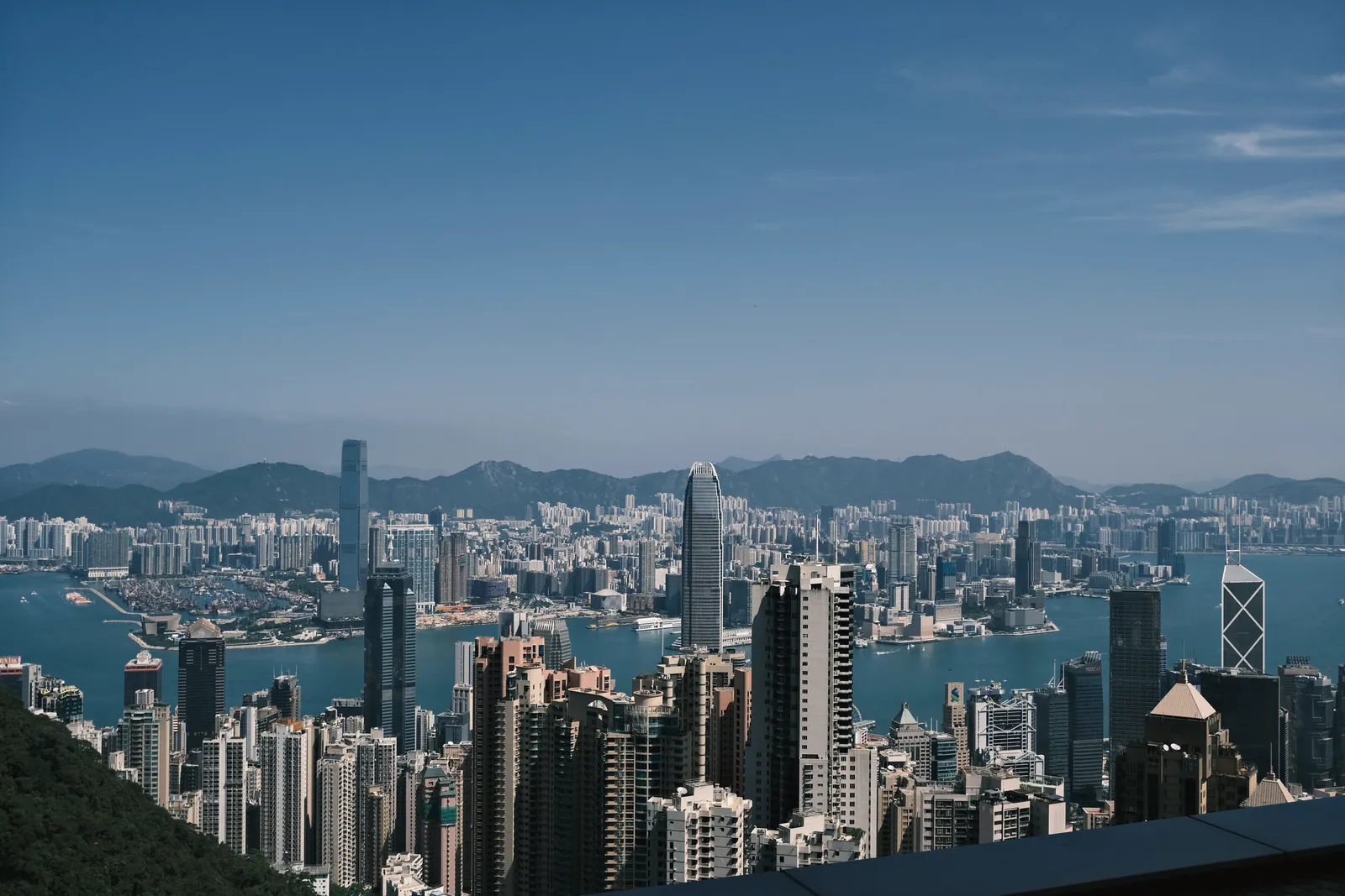 Breathtaking aerial view of Hong Kong's iconic skyline and Victoria Harbour under a clear blue sky.