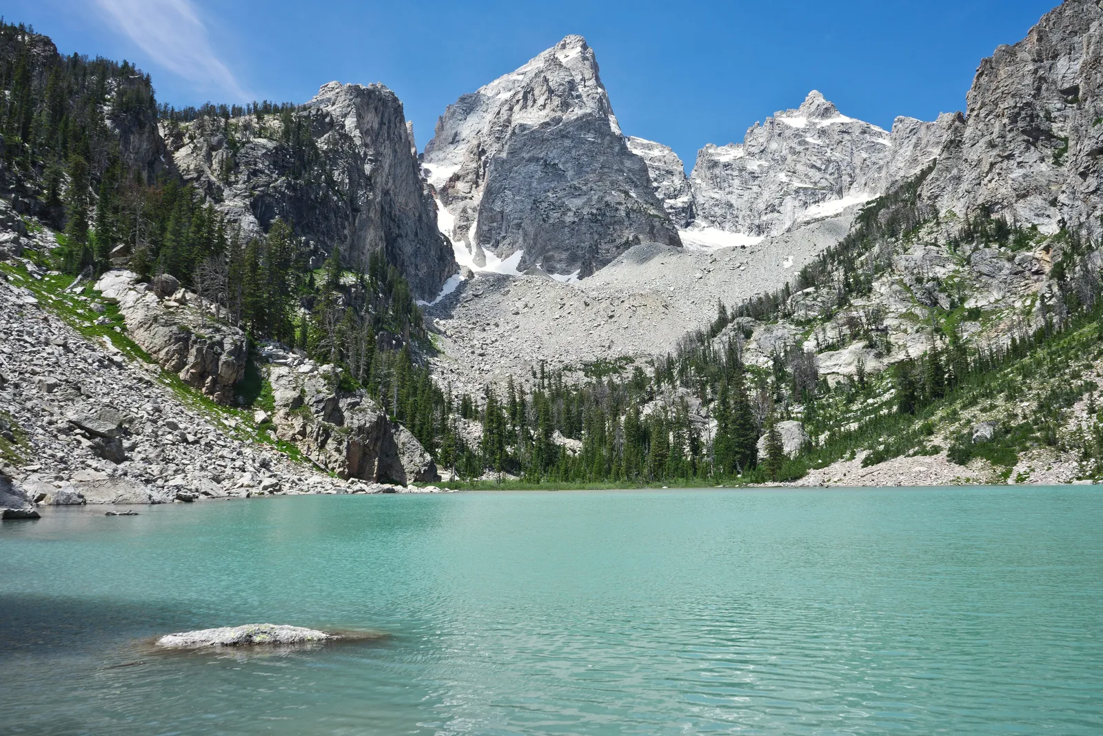 Scenic view of turquoise alpine lake surrounded by towering mountain peaks under clear blue sky.