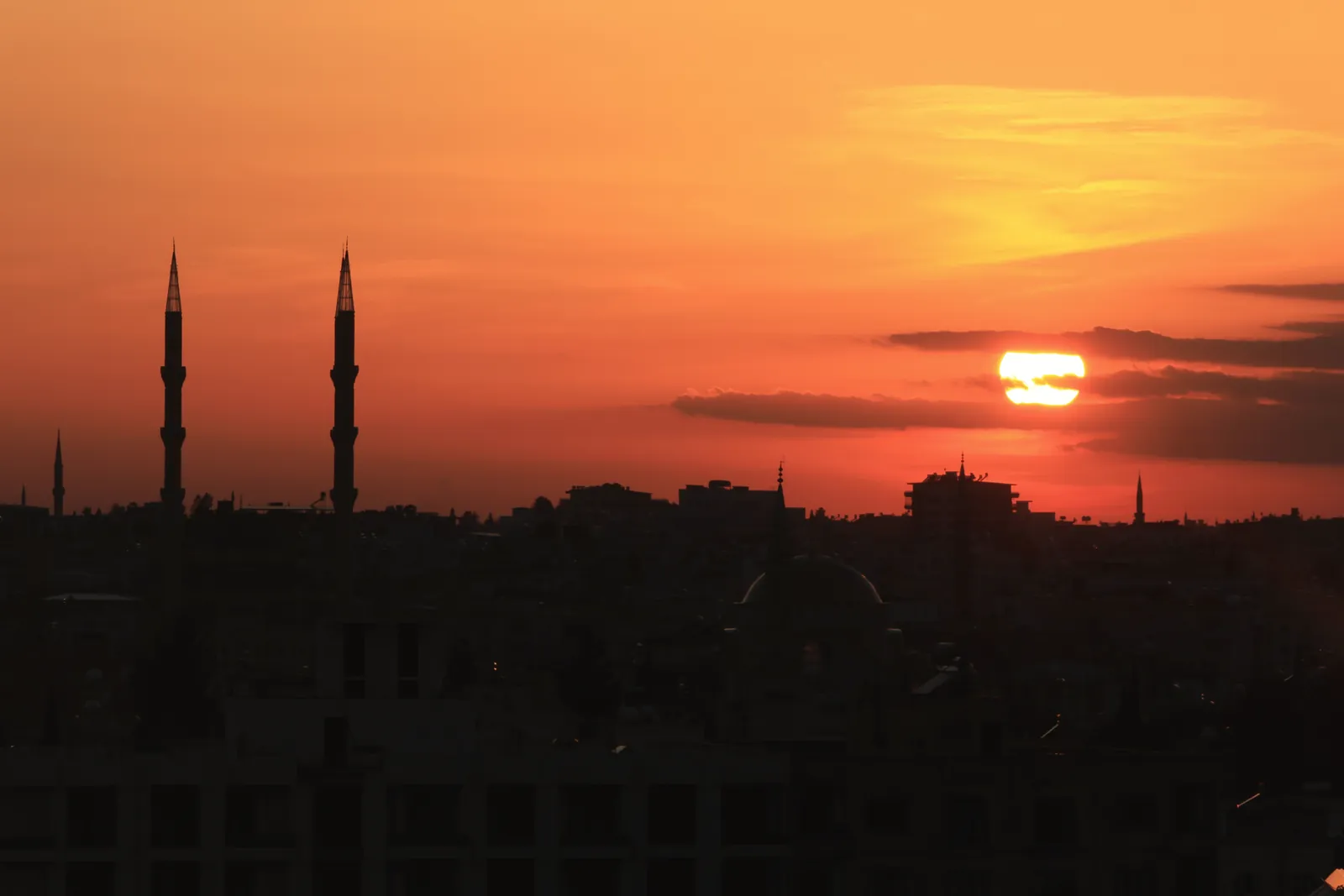 A breathtaking sunset casting an orange hue over a cityscape silhouette with minarets.