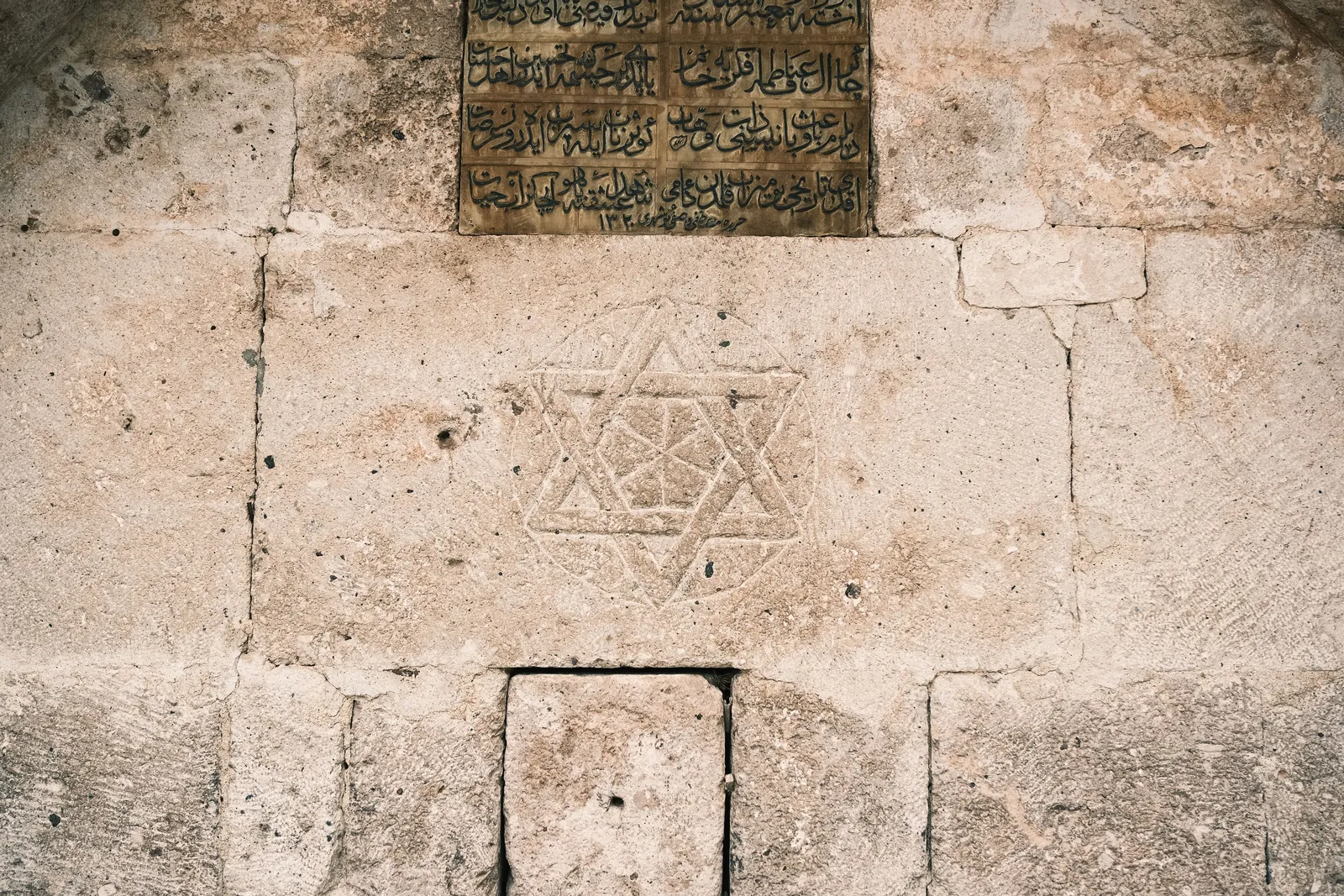 Ancient stone wall featuring a Star of David engraving and Arabic script, highlighting historical architecture.