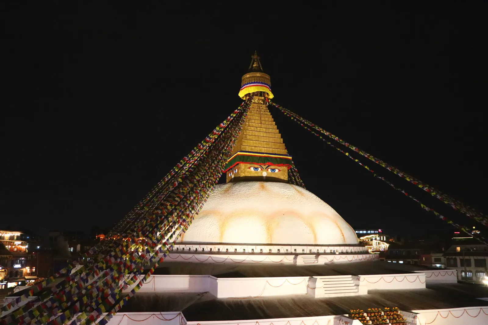 Night view of Boudhanath Stupa in Kathmandu, beautifully illuminated and adorned with prayer flags.