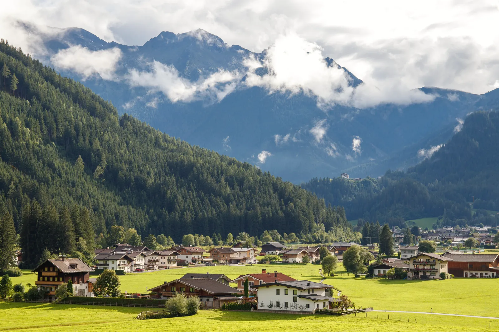 Charming Alpine village nestled against dramatic mountain backdrop under a cloudy sky.