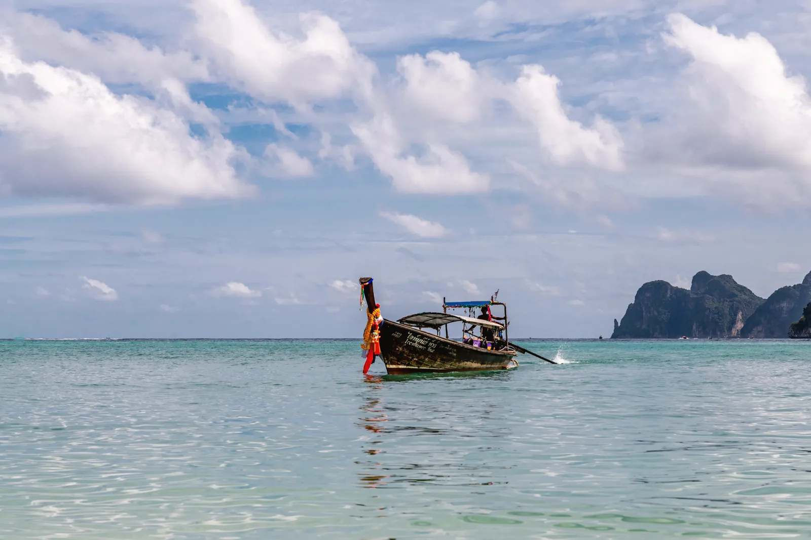 Explore a tranquil scene with a traditional fishing boat off Phuket's coast with serene waters and cloudy skies.
