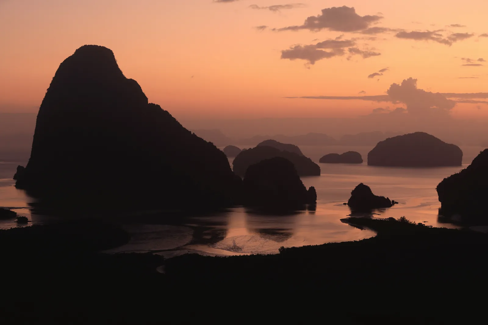 Dramatic silhouettes of rock formations at sunset in Phang-nga Bay, Thailand.