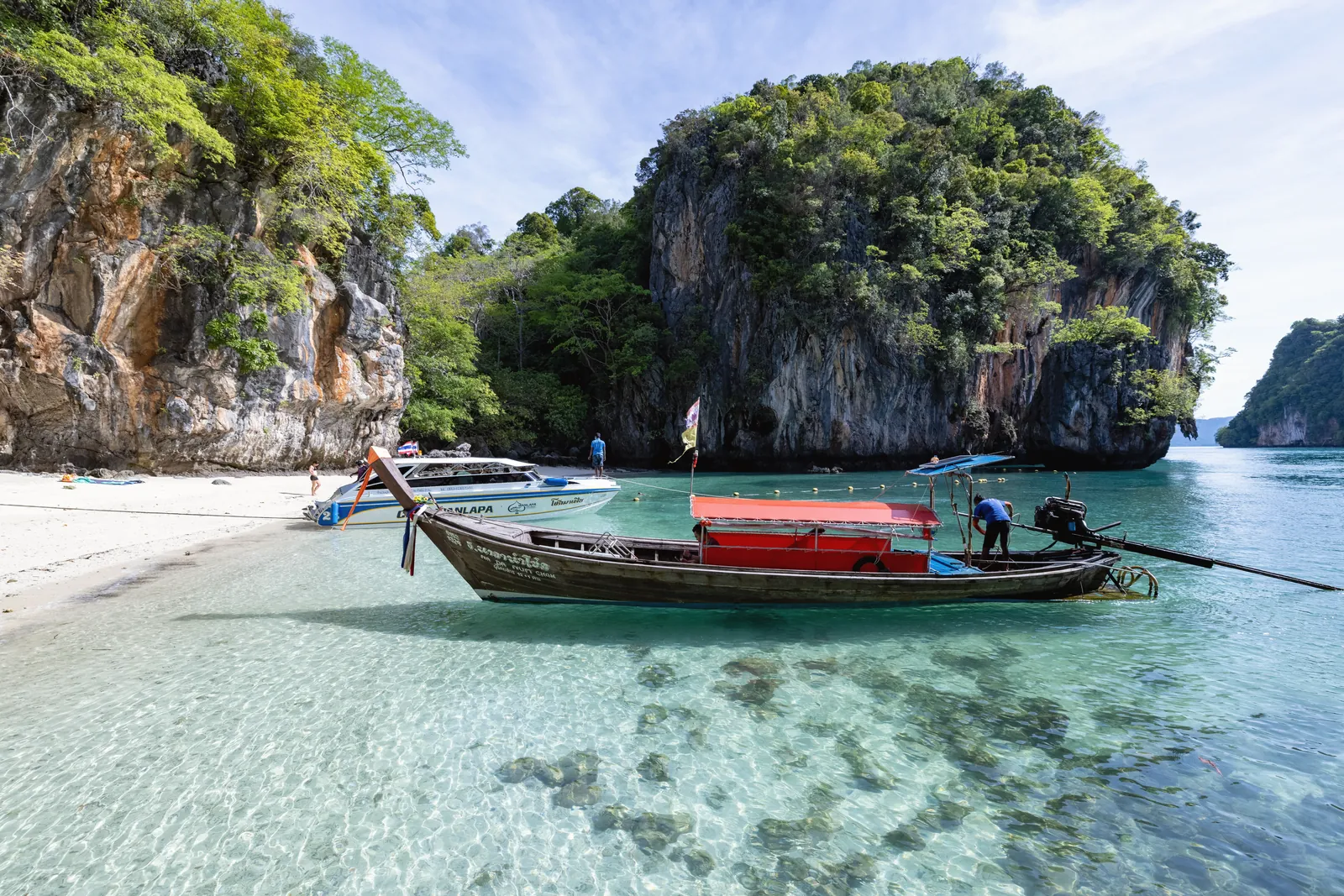 Peaceful Thai beach with clear waters, longtail boat, and limestone cliffs. A perfect tropical escape.