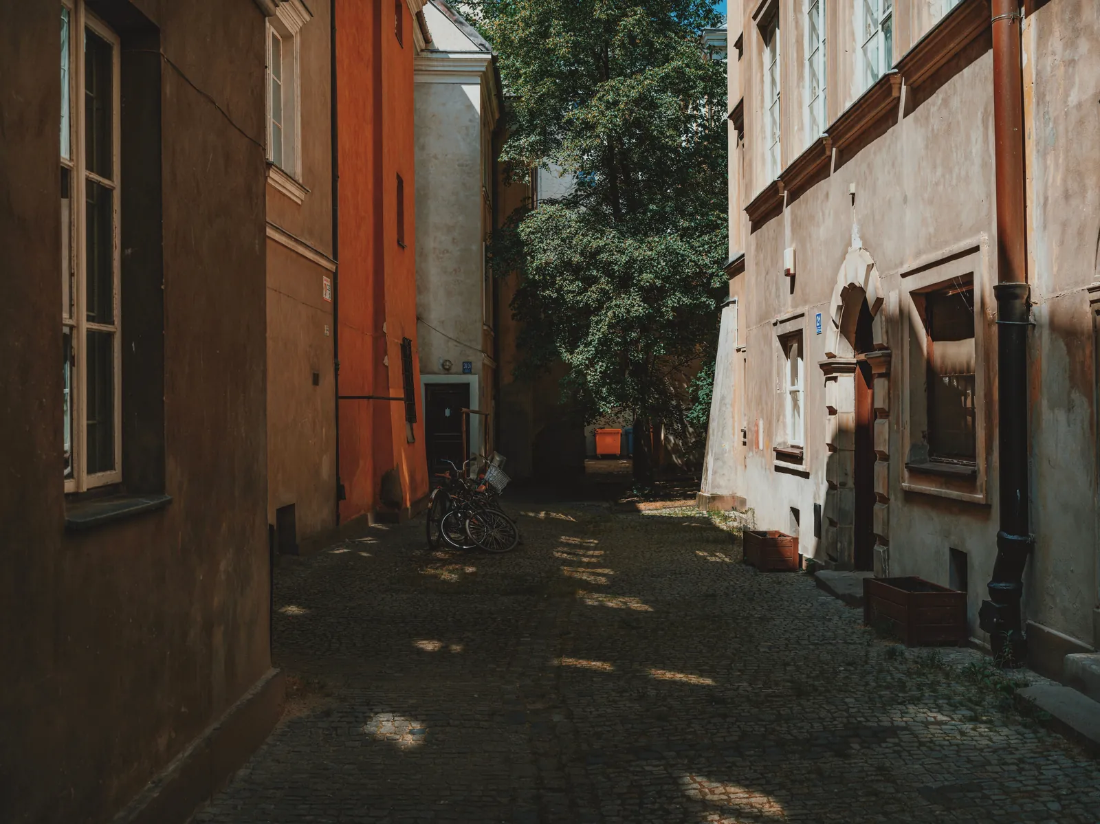 Explore a quiet, sunlit alley in an old town with classic architecture and cobblestone paths.