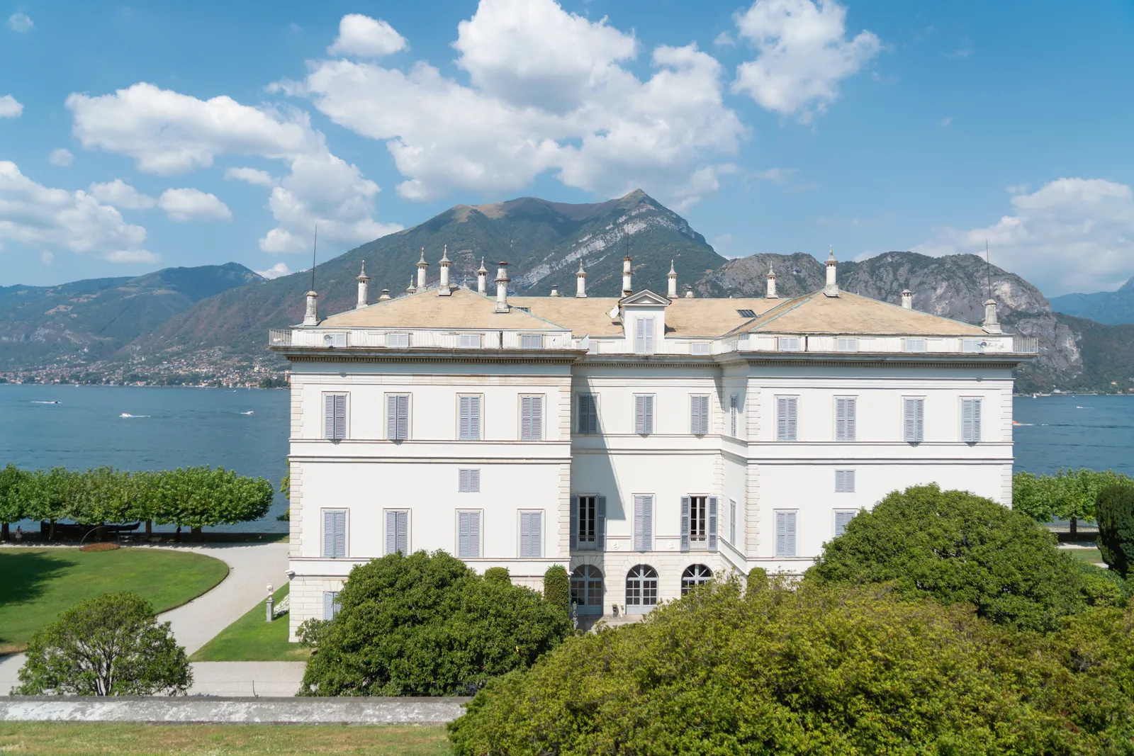 A grand villa surrounded by lush gardens and mountains near the Italian lake.