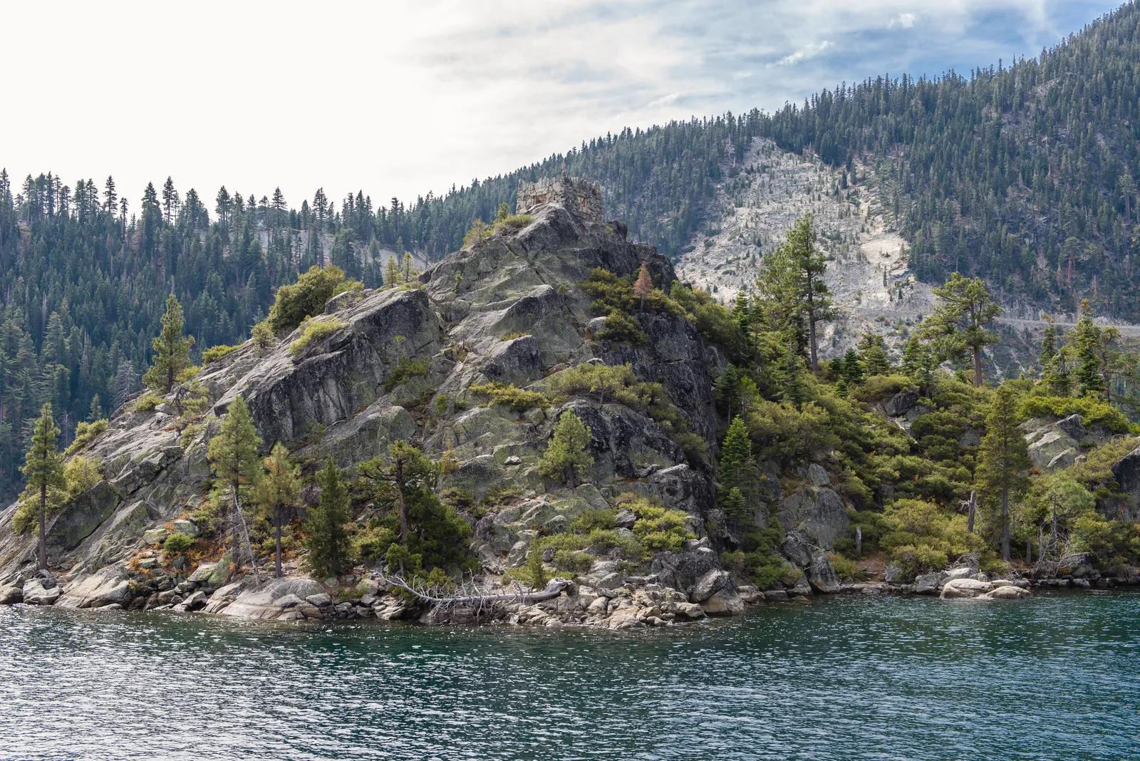 Tranquil view of pine-covered rocky shoreline by calm water body.