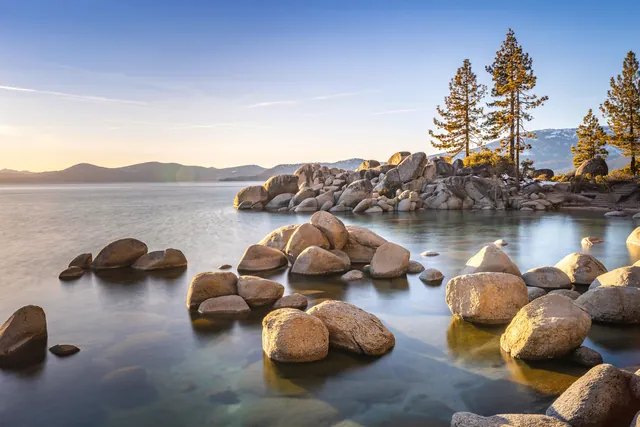 Tranquil sunset view over Lake Tahoe with rocks and pine trees.