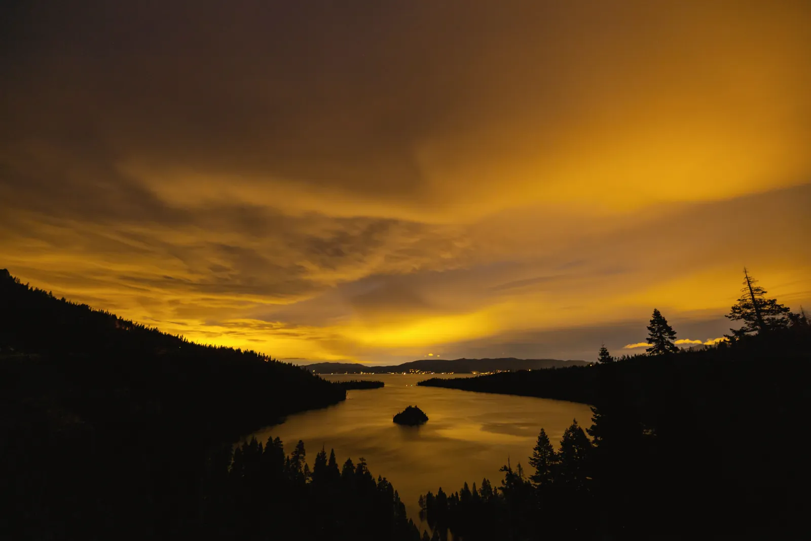 A breathtaking view of a tranquil lake at twilight, framed by silhouetted hills and trees.