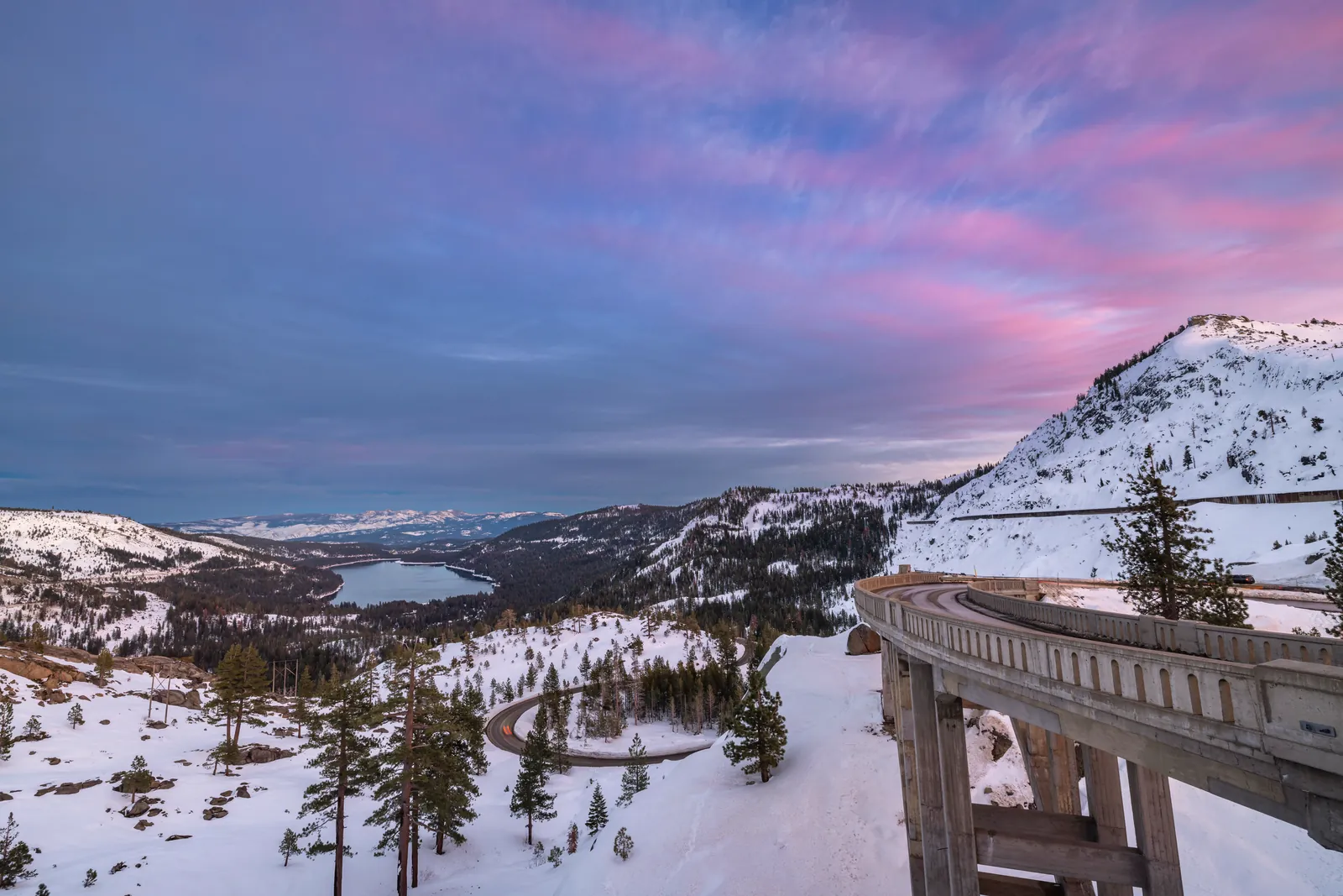 Breathtaking winter landscape of Donner Lake surrounded by snowy Sierra Nevada mountains at sunset.