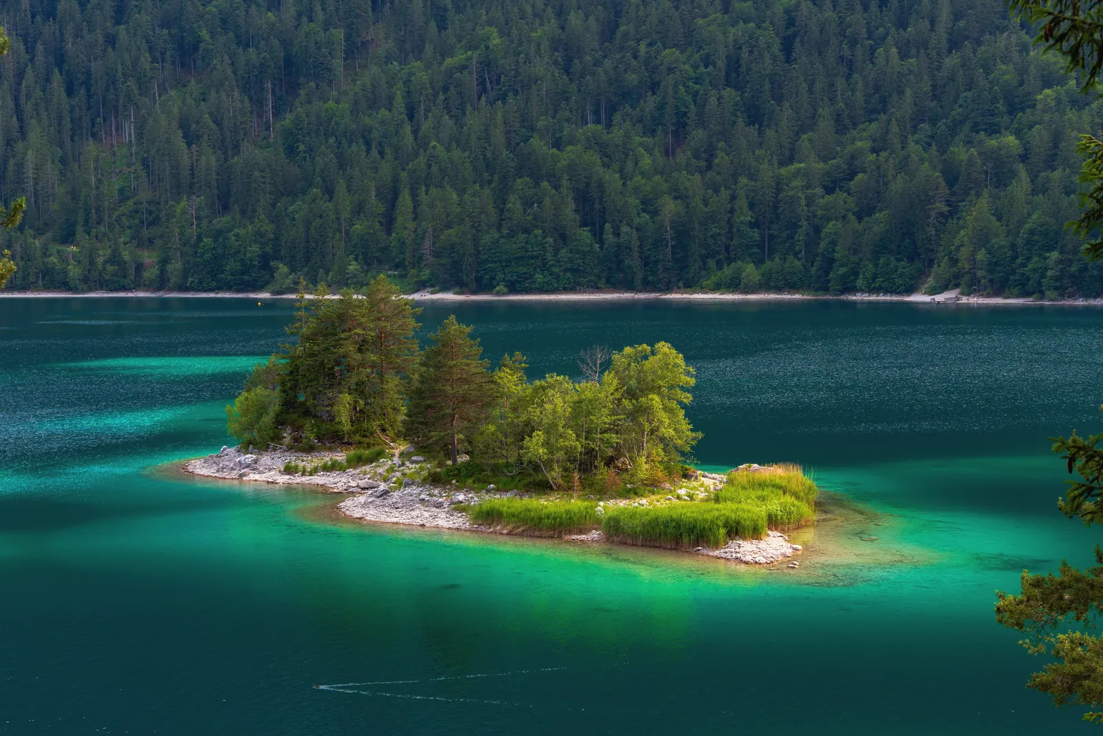 A breathtaking aerial view of a small, lush island in the midst of a tranquil, emerald-colored lake surrounded by dense forest.