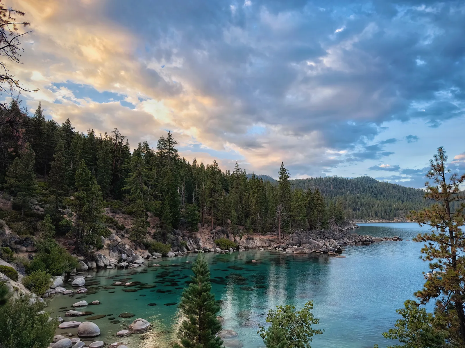 Peaceful Lake Tahoe shoreline with vibrant sunset sky and scenic forested landscape.