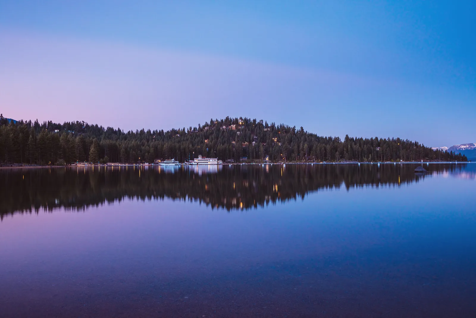 Serene twilight over Lake Tahoe with forested mountain reflections and calm blue waters.