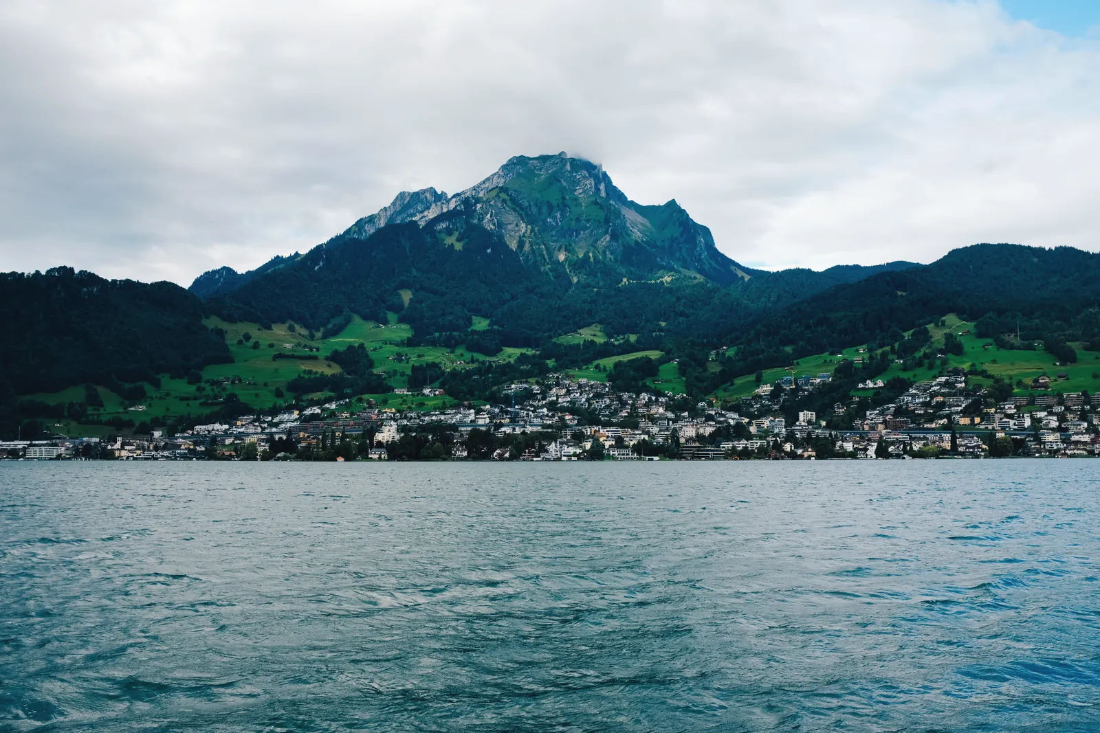 Picturesque lakeside town with majestic mountain backdrop under cloudy sky.